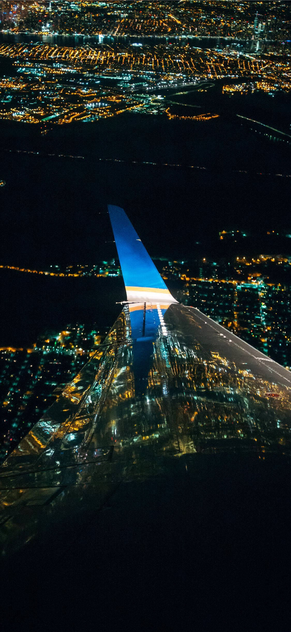 飛機 桌布 壁紙 — 夜間飛機翼翱翔於無數溫暖燈光照耀下閃爍城市景觀的鳥瞰圖。