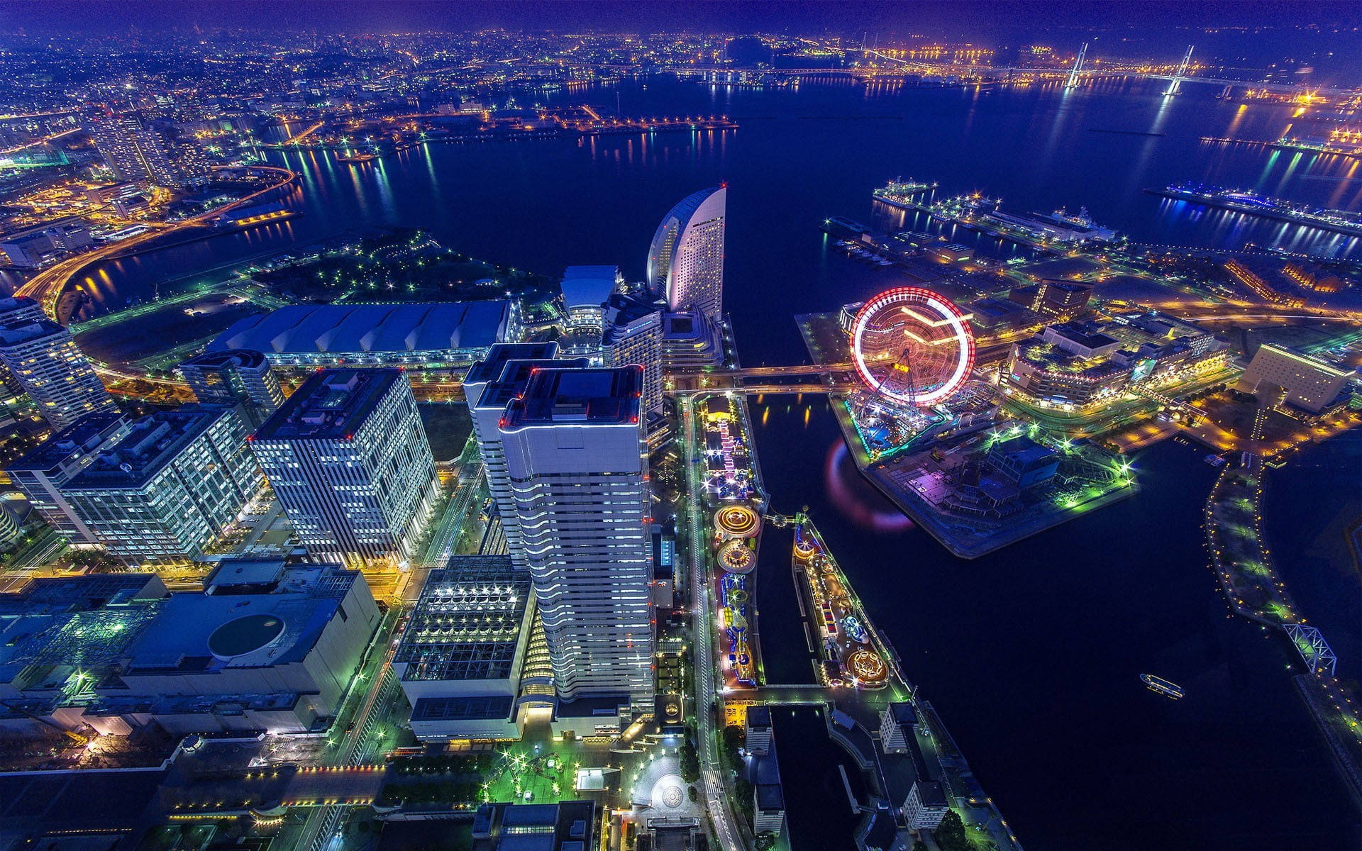 Yokohama 桌布 壁紙 — 夜間鳥瞰充滿活力的城市景觀，閃爍的摩天大樓和色彩繽紛的摩天輪旁邊是一條黑暗的水道。