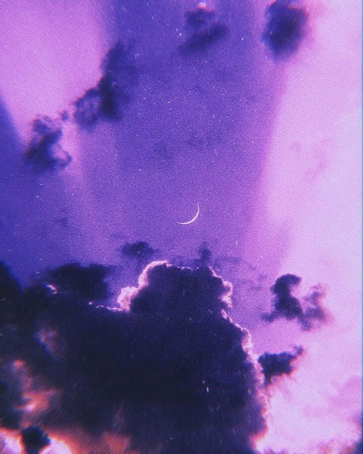 紫色美學 桌布 壁紙 — 夢幻的紫色天空，帶有新月和暗雲，邊緣閃爍著粉紅色和橙色。