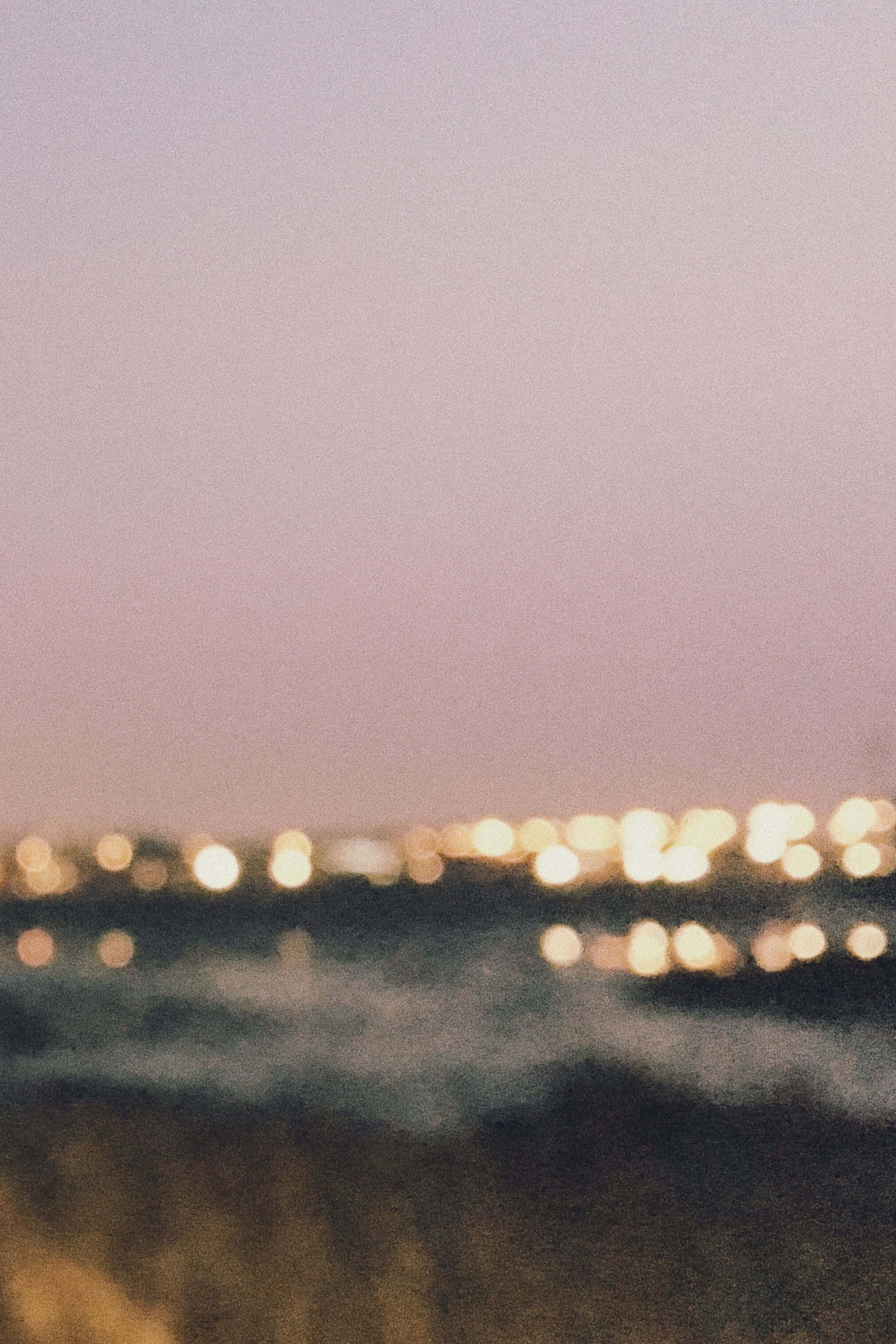 美學 桌布 壁紙 — 夢幻的黃昏場景，模糊的城市燈光在深色水面上柔和發光，下方是粉紫色天空。