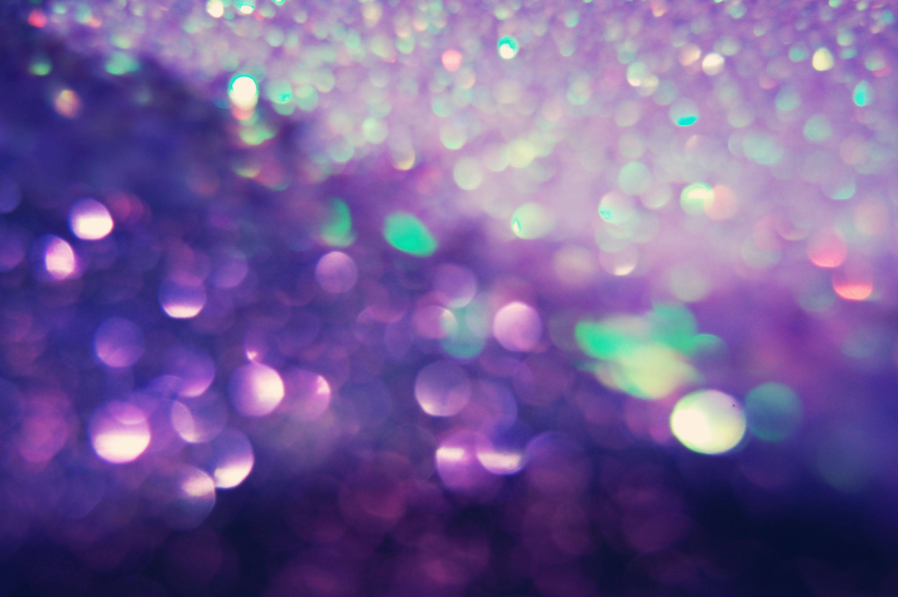 Purple Glitter 桌布 壁紙 — 夢幻般的散景效果，閃爍的紫色和藍綠色亮粉粒子在深色背景上柔和發光。