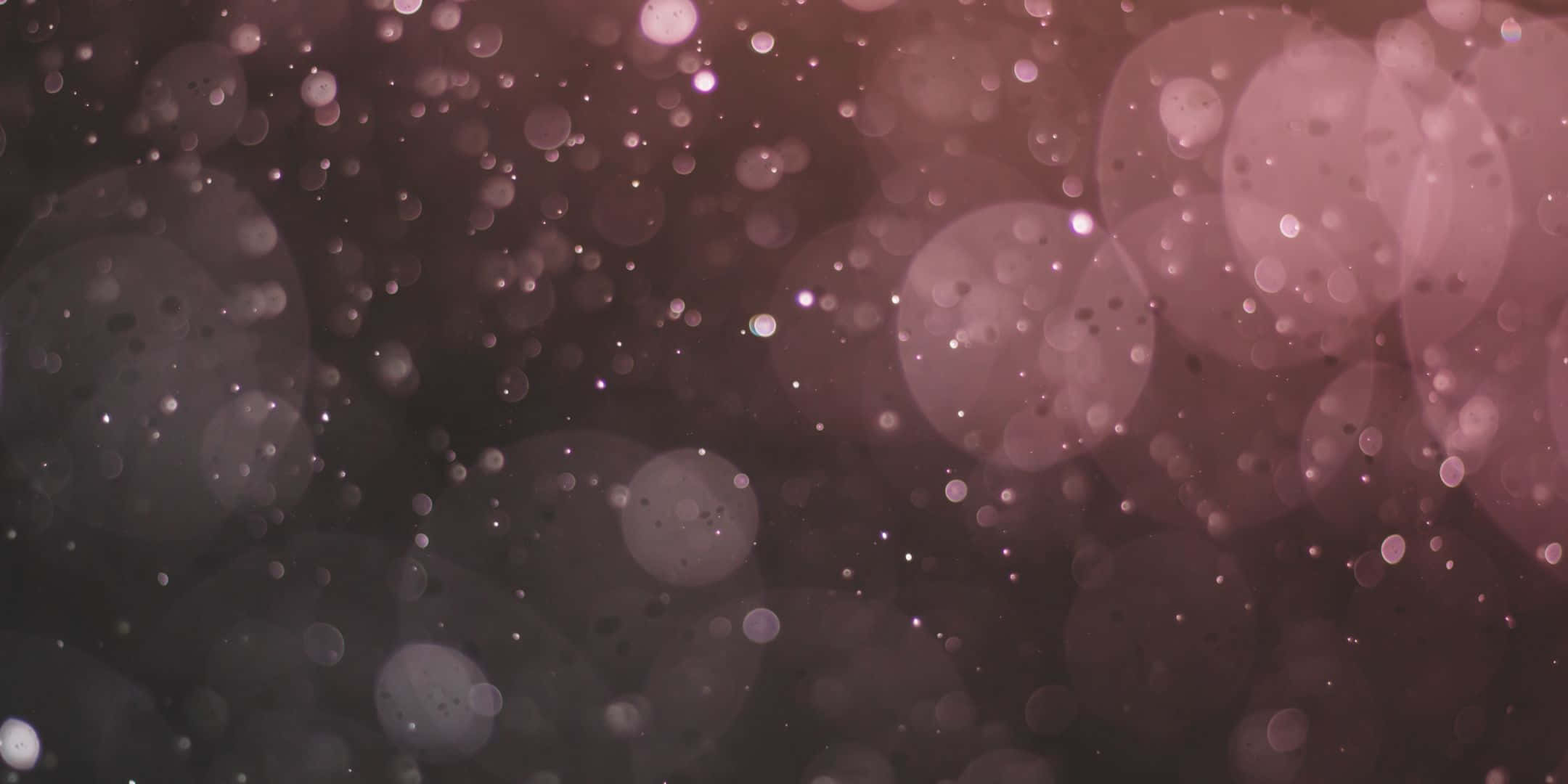 Shimmer 桌布 壁紙 — 夢幻般的散景背景，帶有柔和的粉紅色和紫紅色發光球體，以及漂浮在黑暗中的閃爍粒子。