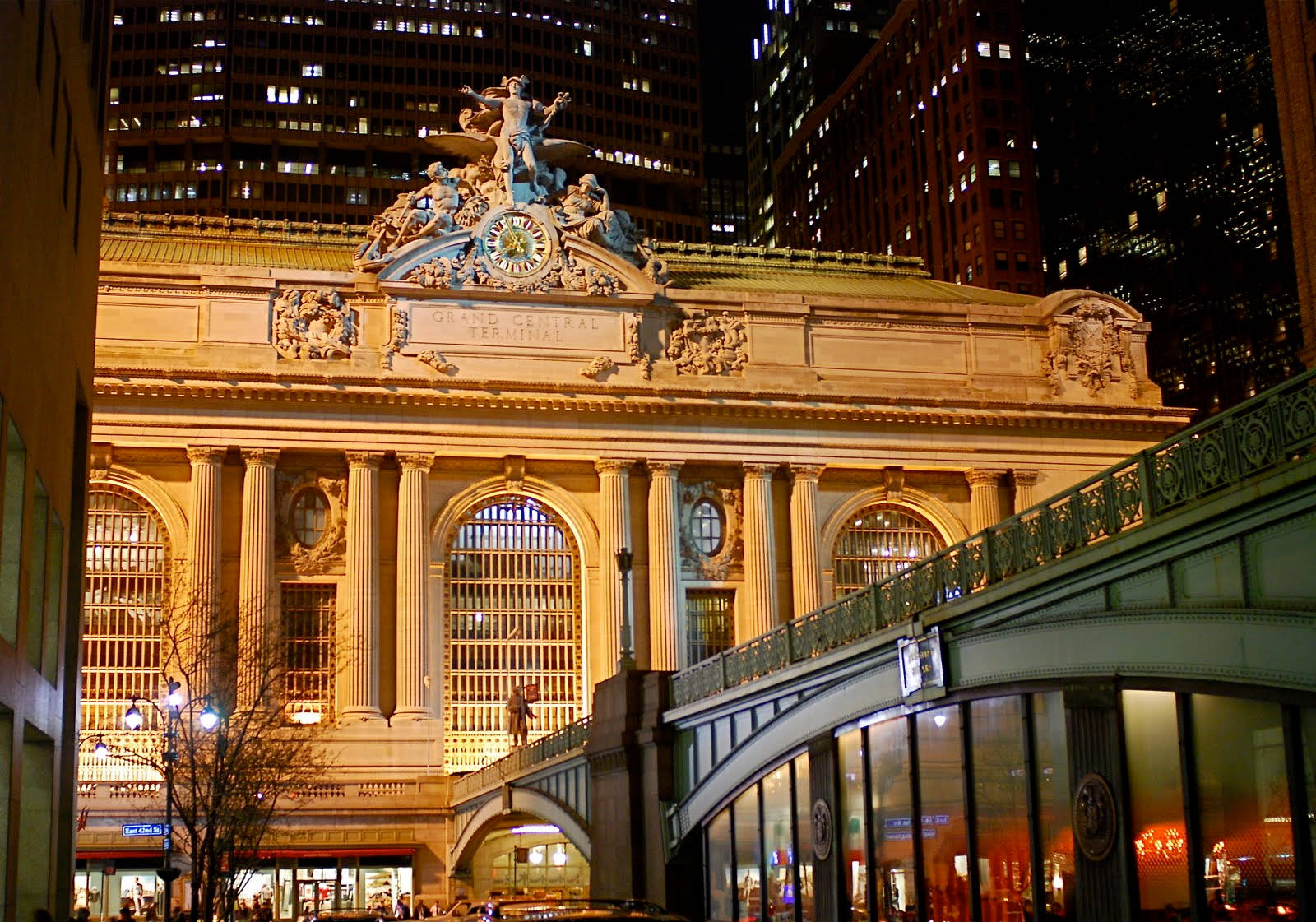 New York 桌布 壁紙 — 大中央車站在夜晚被溫暖的金色燈光照亮，映襯著黑暗的城市摩天大樓。