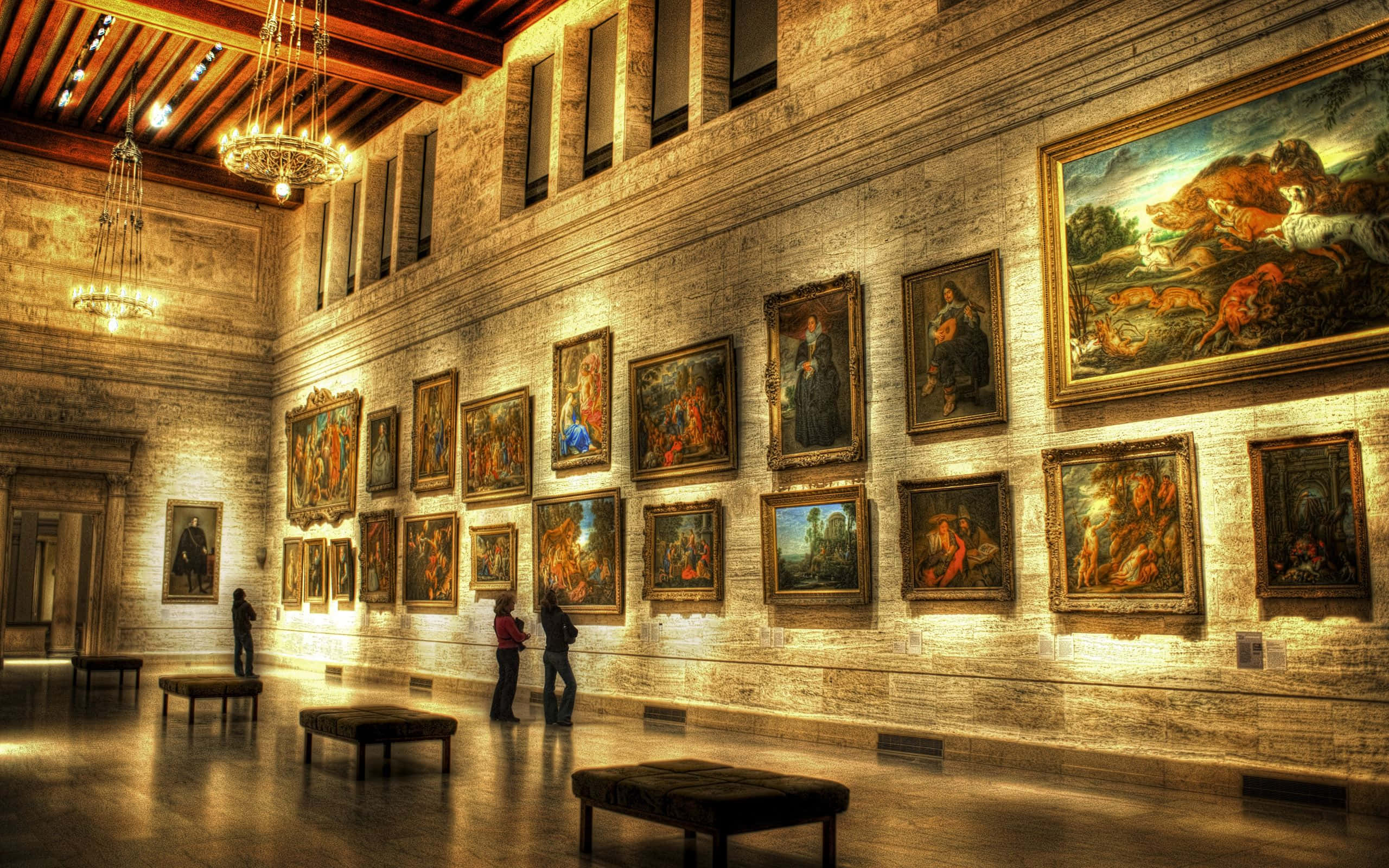 Museums 桌布 壁紙 — 大型博物館畫廊，高天花板和石牆，在溫暖的吊燈下展示眾多古典畫作。