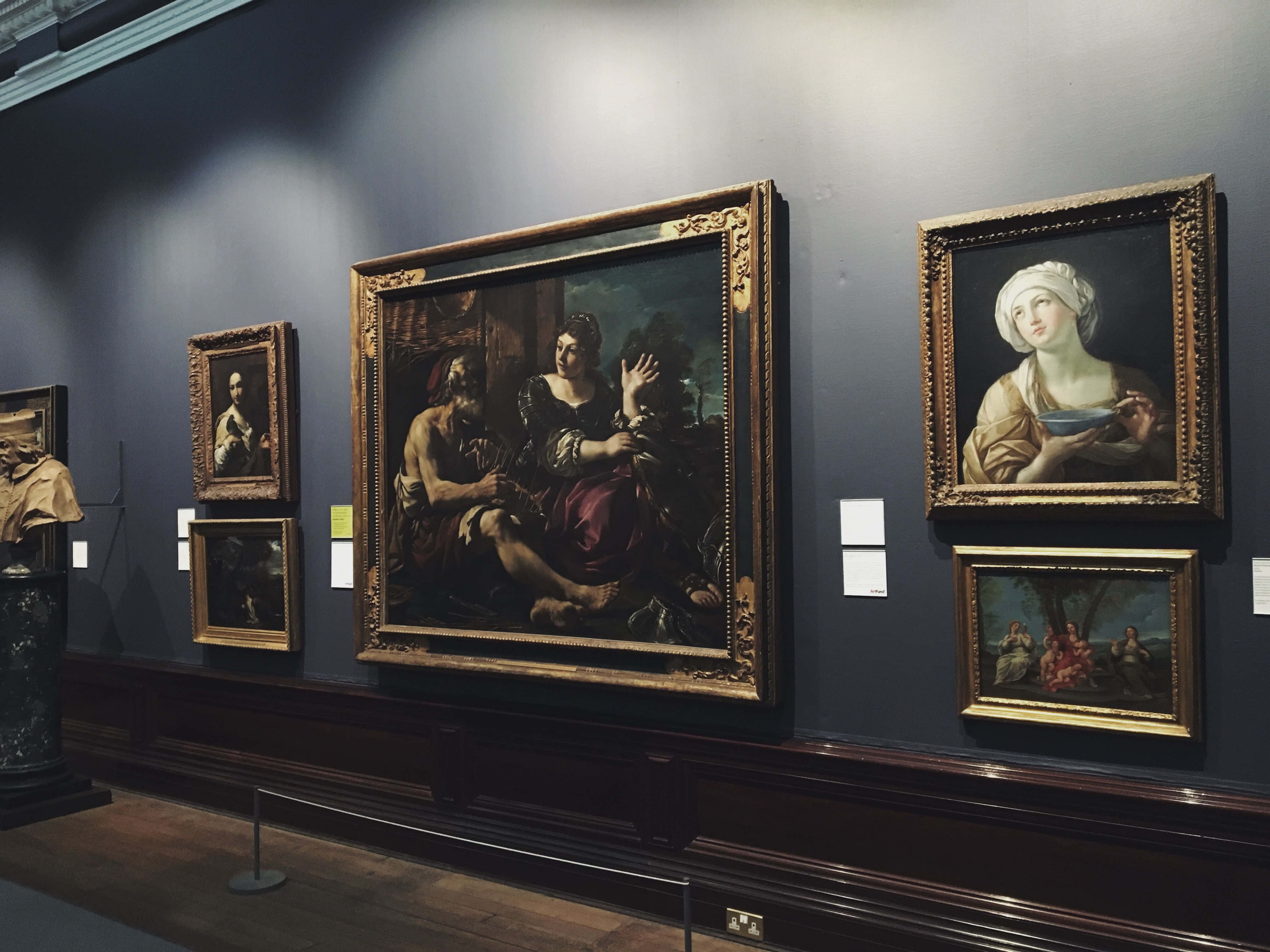 Museums 桌布 壁紙 — 大型古典畫作鑲在華麗的金色畫框中，掛在深藍色的畫廊牆上，聚光燈聚焦照射。