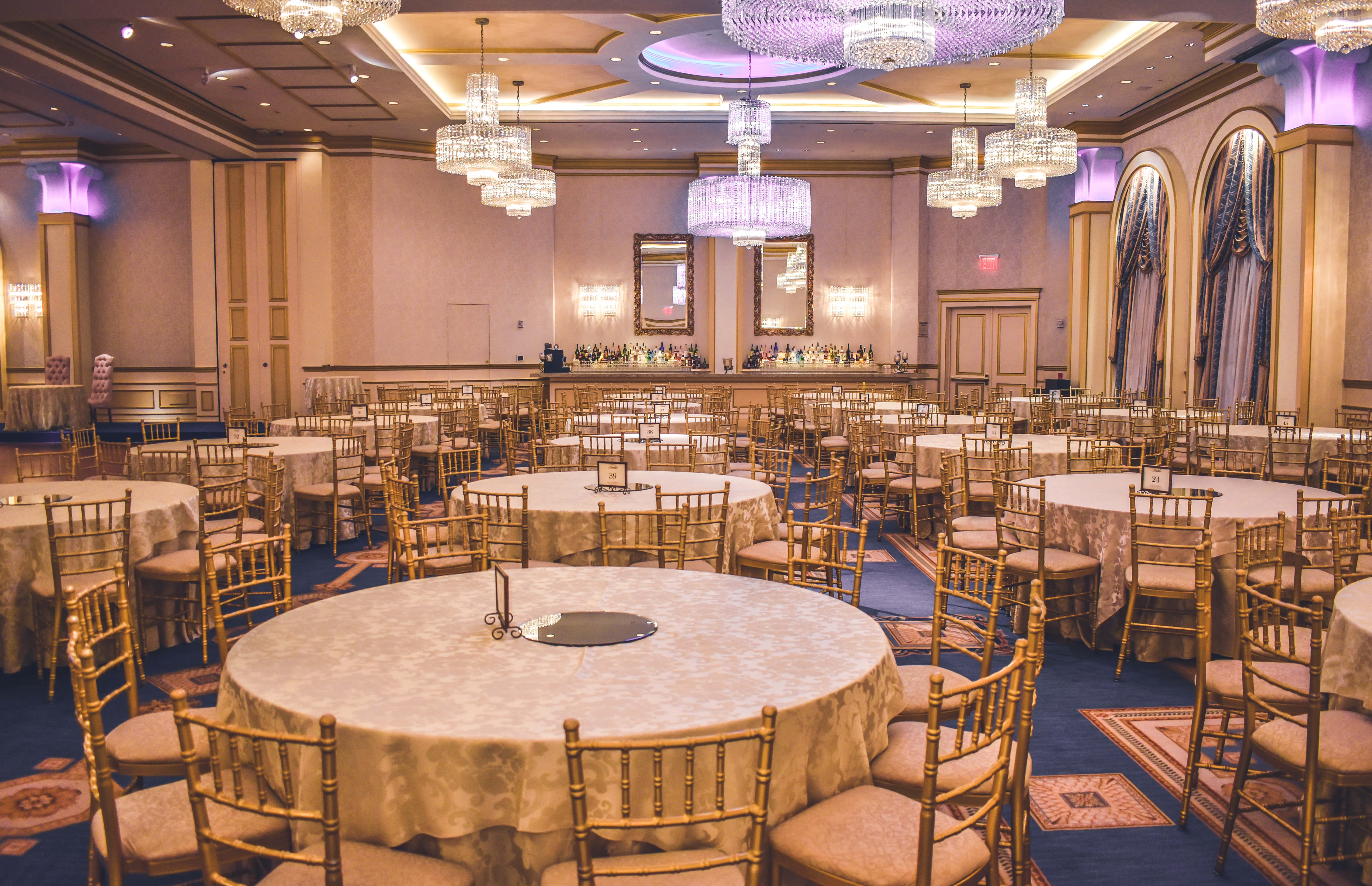 Ballroom 桌布 壁紙 — 大型宴會廳，設有圓桌、金色 Chiavari 椅子和水晶吊燈，配以紫色環境燈光。