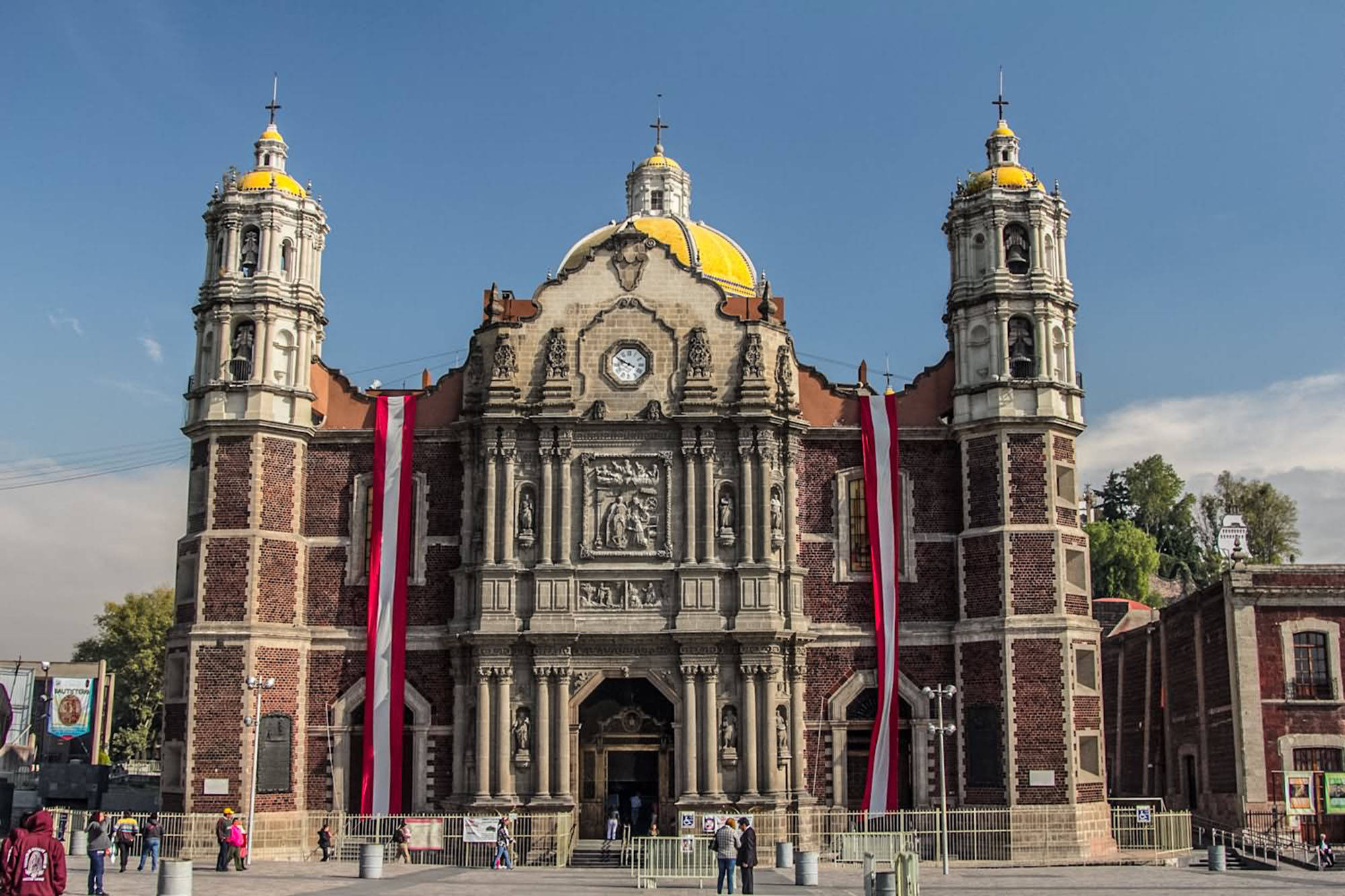 Church 桌布 壁紙 — 大型殖民教堂，雙鐘樓和金色圓頂，在晴朗藍天下，紅色橫幅垂掛在前方。