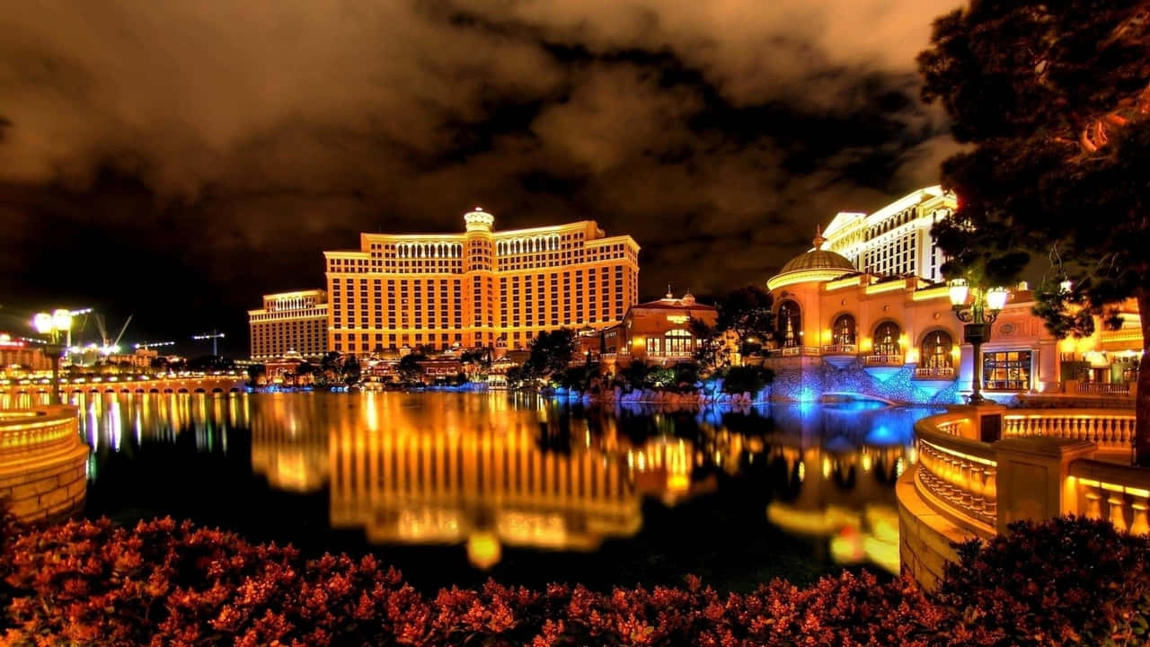720p Las Vegas 桌布 壁紙 — 大型燈光璀璨的度假村建築在平靜的水道上倒映，上方是帶有烏雲的戲劇性夜空。