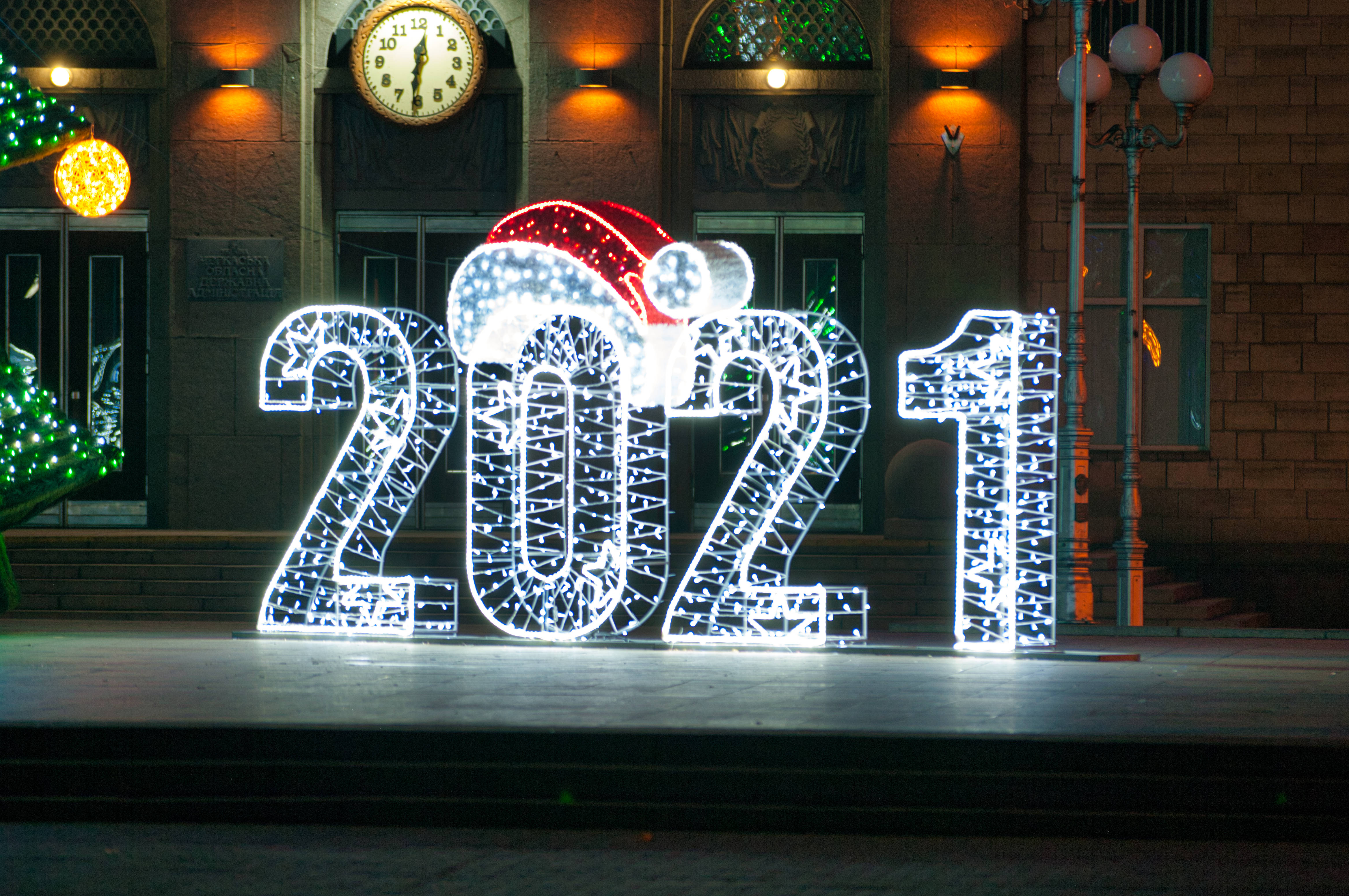 新年快樂 桌布 壁紙 — 大型發光2021數字戴著聖誕帽，在夜晚的磚砌建築前明亮地發光。