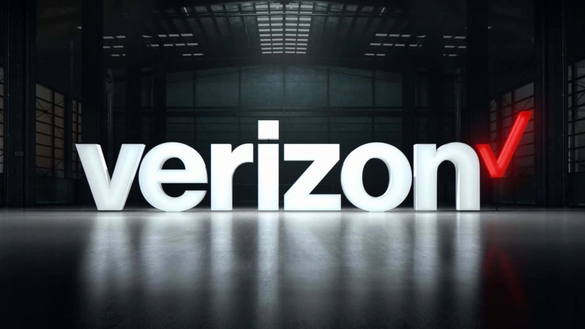 威訊 桌布 壁紙 — 大型發光白色Verizon標誌帶紅色勾號，位於黑暗工業倉庫中央，地板有反射效果。