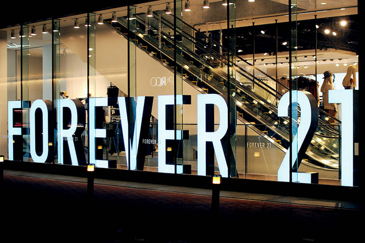 永遠21 桌布 壁紙 — 大型發光的「FOREVER 21」字母照亮了夜晚的玻璃門面商店，內部可見電扶梯和模特兒。