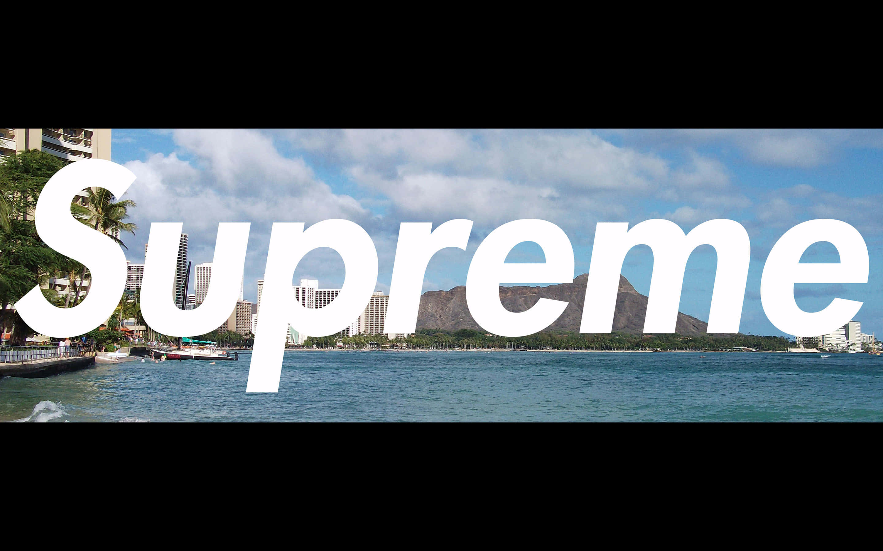 supreme 桌布 壁紙 — 大型白色 'Supreme' 標誌覆蓋在海岸城市景觀上，有藍綠色海水、棕櫚樹和遠處的山脈，天空部分多雲。