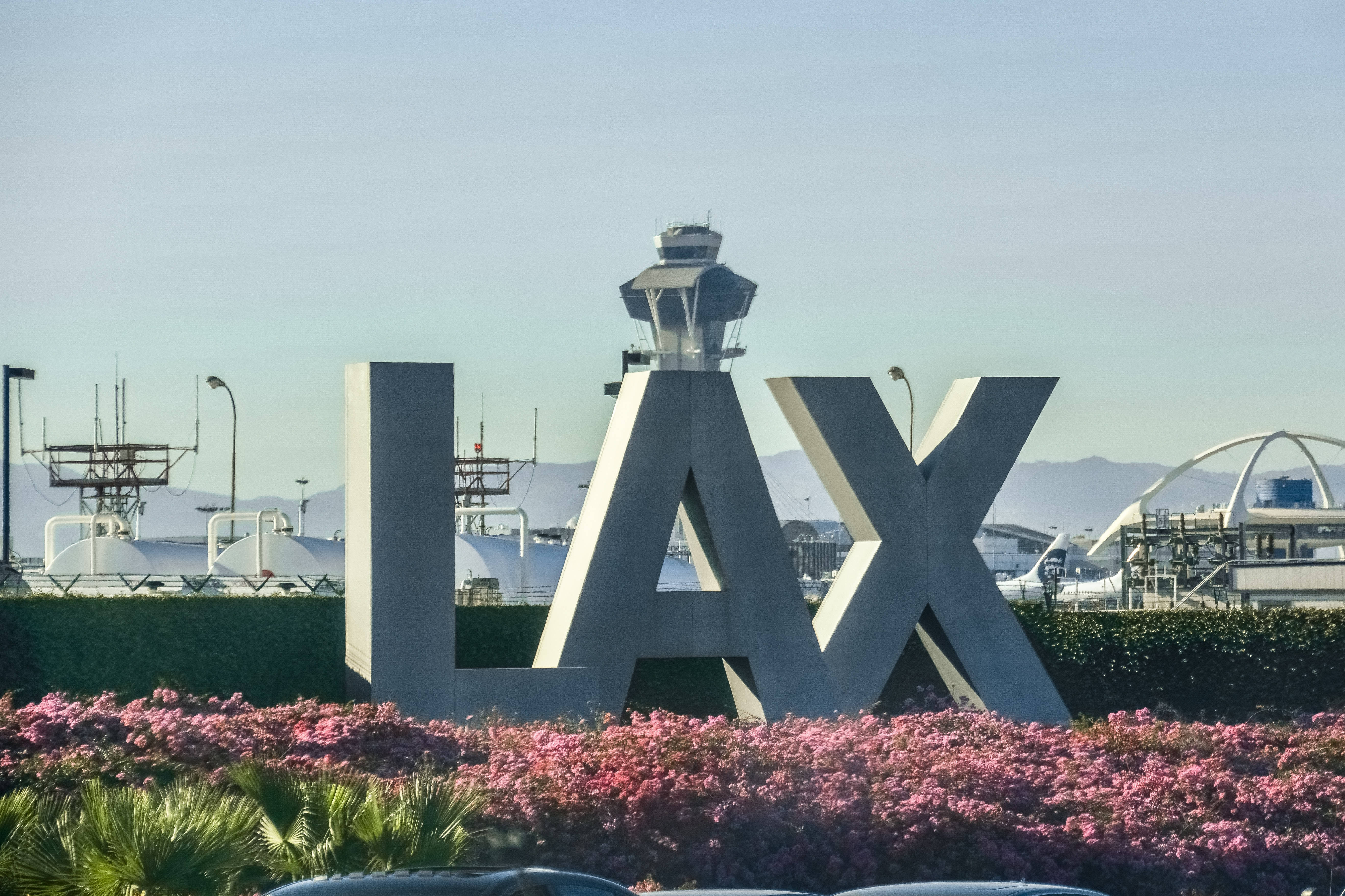 Airport 桌布 壁紙 — 大型白色LAX字母矗立在控制塔前，前景有粉紅色開花灌木，背景是清澈的藍天。