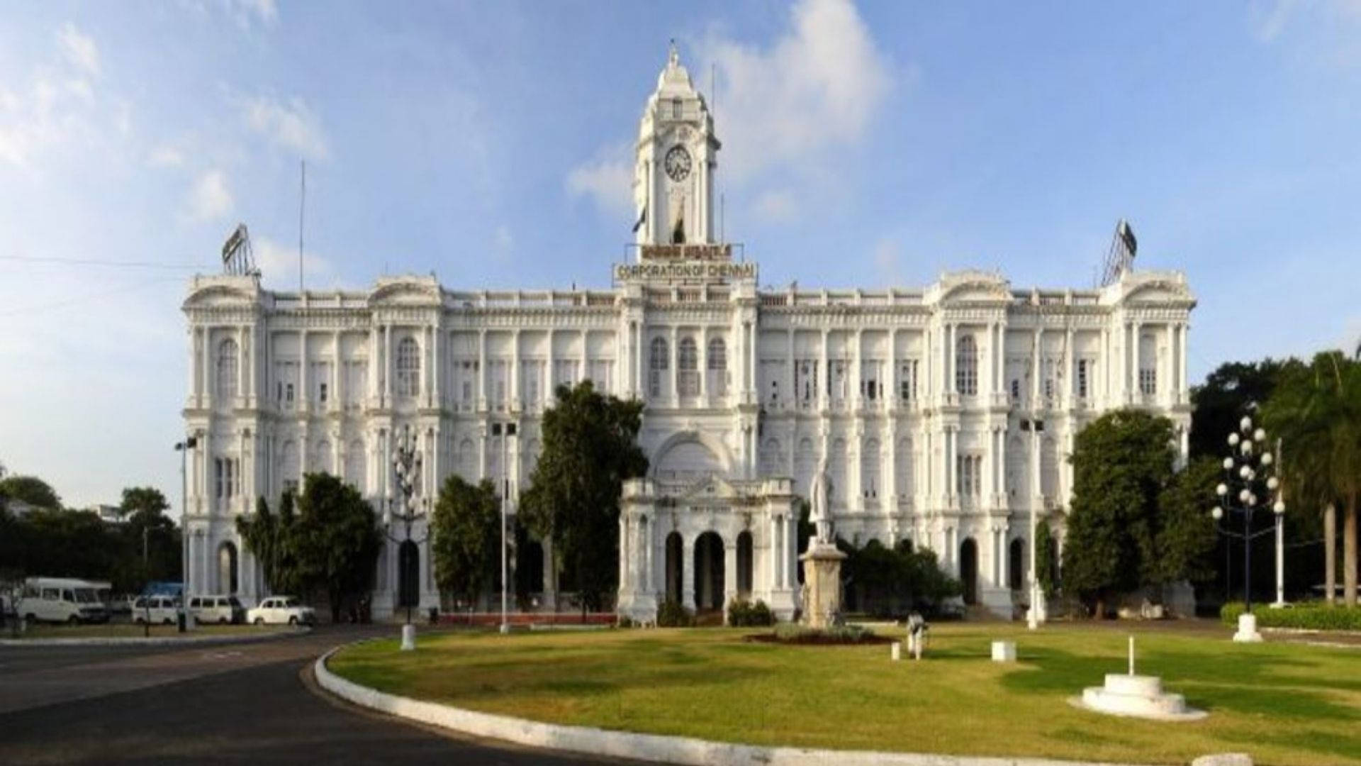 Chennai 桌布 壁紙 — 大型白色殖民時代政府建築物，帶有鐘樓，矗立在明亮的藍天下，周圍環繞著綠色草坪和樹木。