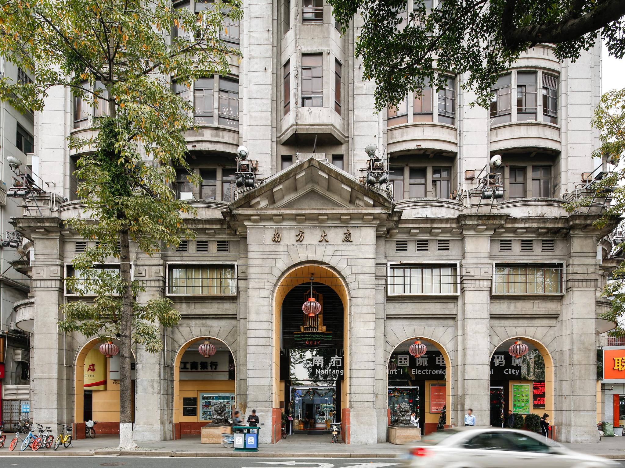 Guangzhou 桌布 壁紙 — 大型石面建築，設有拱形入口和中文字，周圍環繞著茂密的綠樹和一輛經過的汽車。