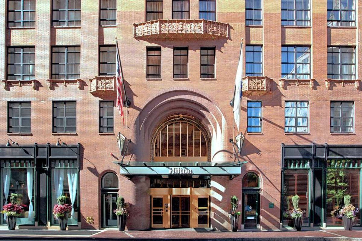 Building 桌布 壁紙 — 大型磚砌飯店外牆，拱形入口和旗幟在明亮日光下。