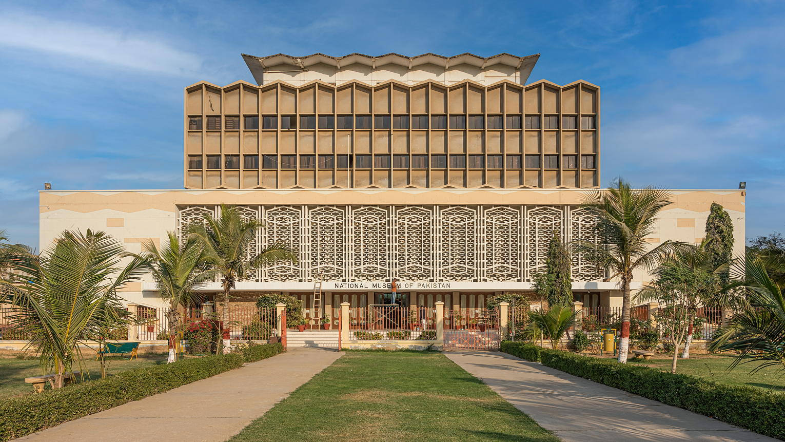 Karachi 桌布 壁紙 — 大型米色巴基斯坦國家博物館矗立在晴朗藍天下，棕櫚樹和修剪整齊的草坪環繞著中央步道。