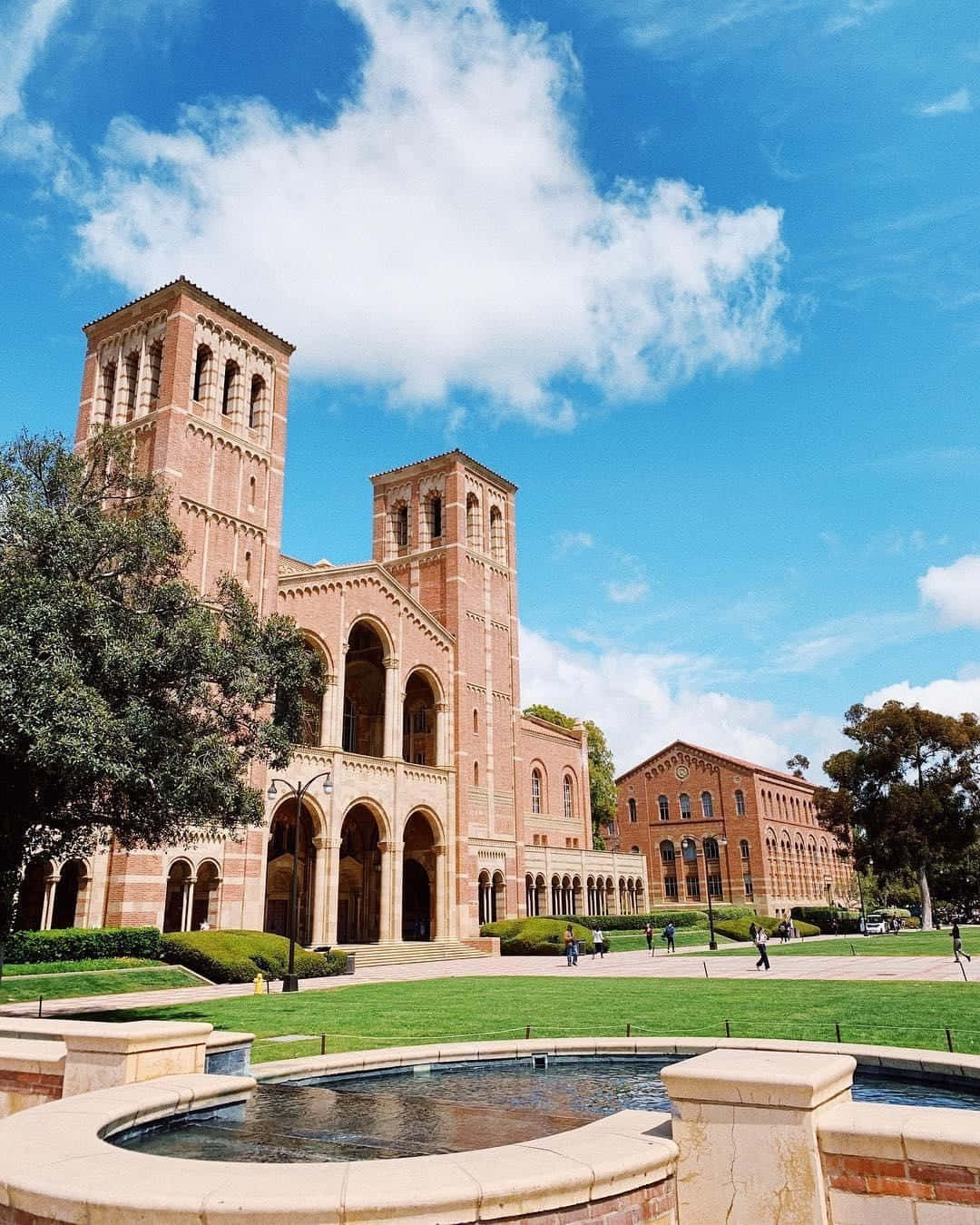 Ucla Campus 桌布 壁紙 — 大型紅磚大學建築，設有拱形步道和塔樓，在晴朗藍天和蓬鬆白雲下。