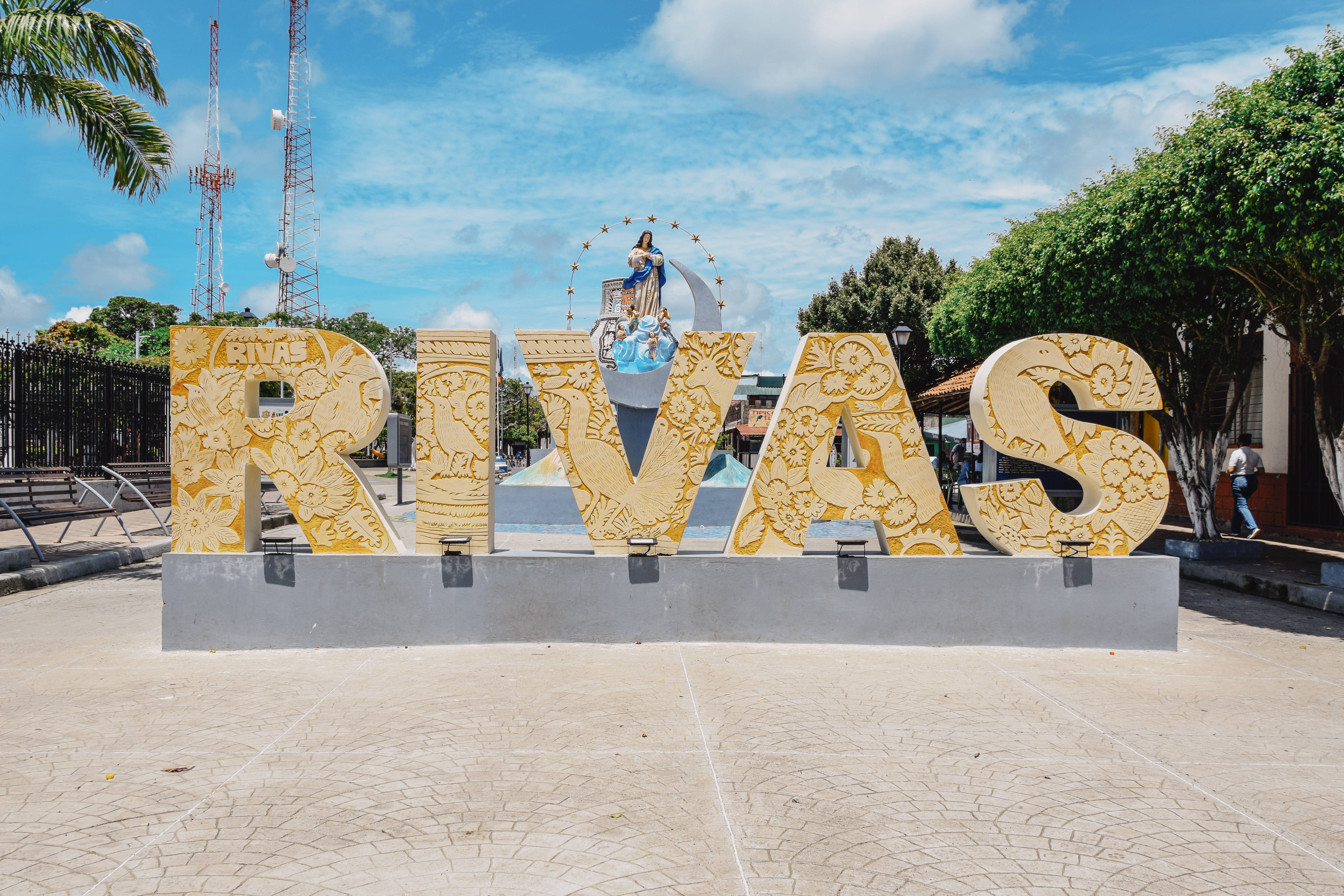 Nicaragua 桌布 壁紙 — 大型華麗金色字母拼出RIVAS，矗立在陽光普照的廣場上，藍天白雲。