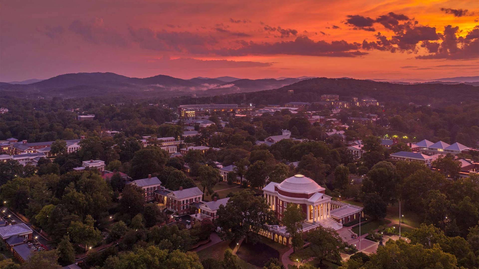 Virginia 桌布 壁紙 — 大學校園日落時分的鳥瞰圖，火紅色的天空和燈火通明的建築物隱藏在茂密的綠樹之中。