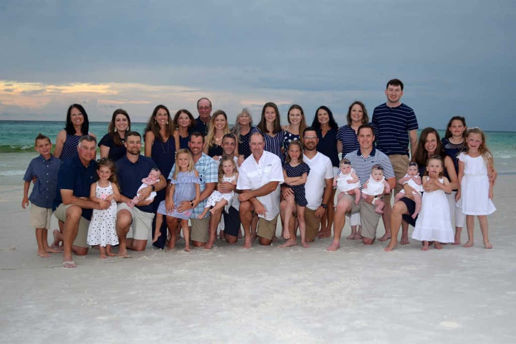 Beach Family 桌布 壁紙 — 大家庭在沙灘上一起擺姿勢，背景是日落、海浪和多雲的天空。