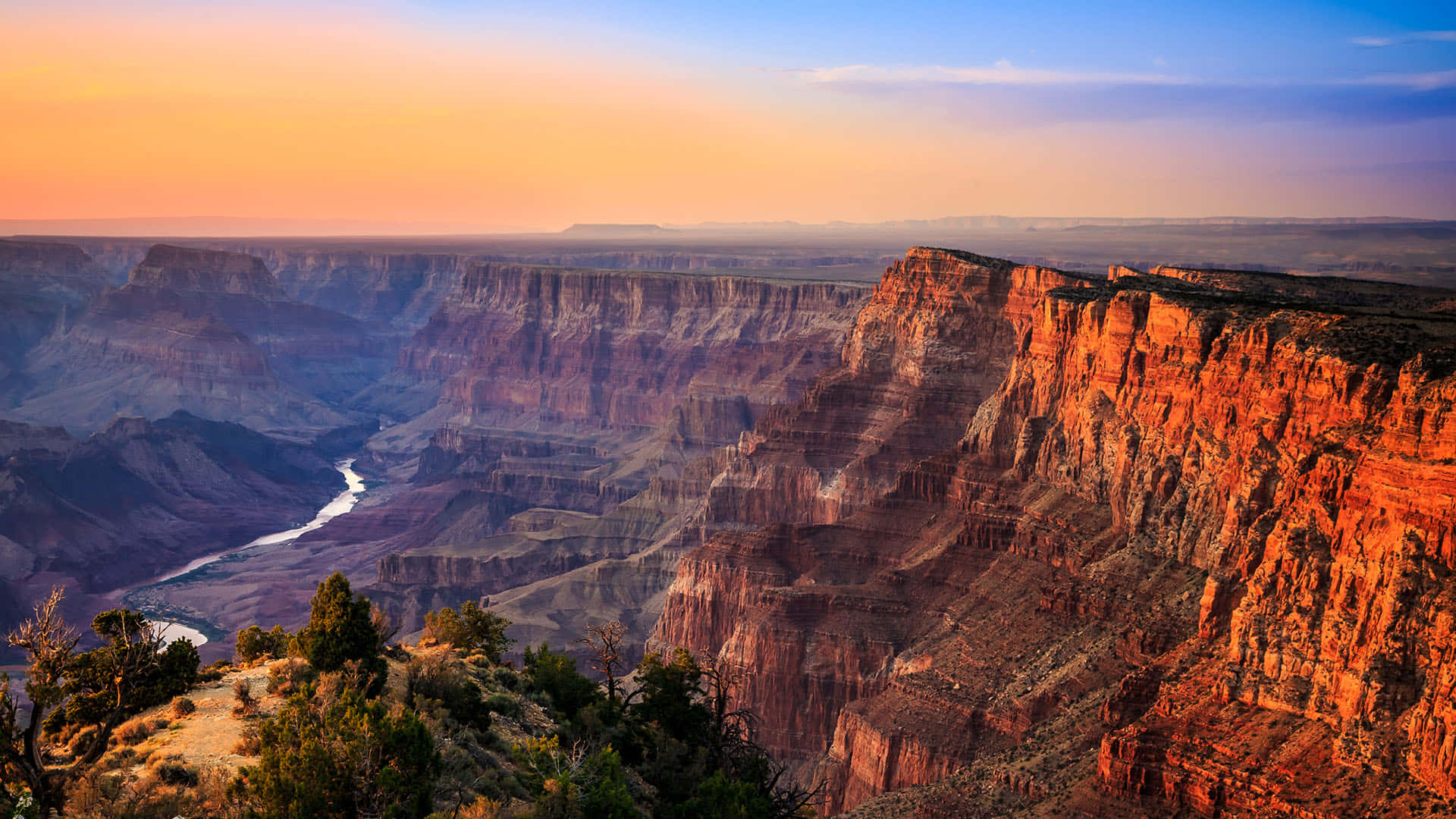 grand canyon 桌布 壁紙 — 大峽谷沐浴在金色夕陽下，層層疊疊的紅色岩石懸崖和下方蜿蜒的河流。