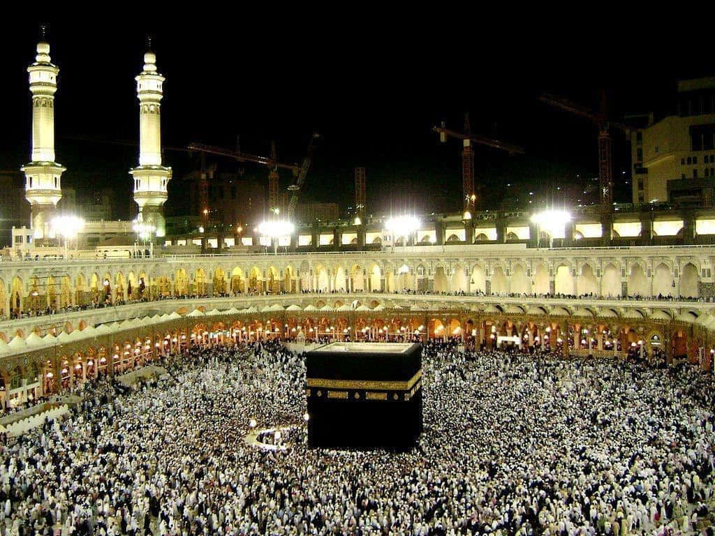 Makkah 桌布 壁紙 — 大批身穿白衣的朝聖者在麥加夜晚的明亮燈光下圍繞著黑色天房。