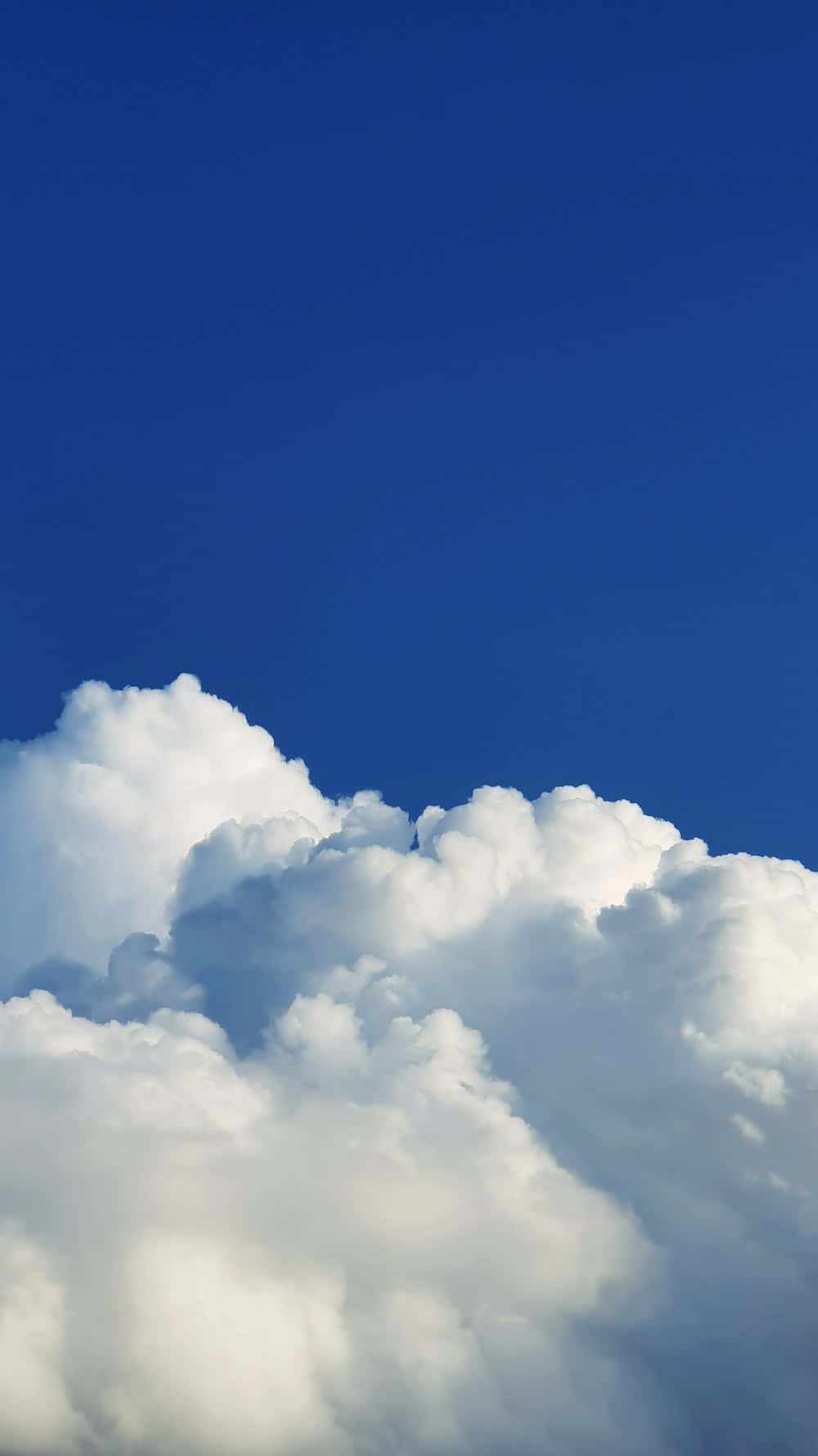 Minimalist Sky 桌布 壁紙 — 大片蓬鬆的白雲在深寶藍色的天空中飄浮，呈現寧靜的自然景象。