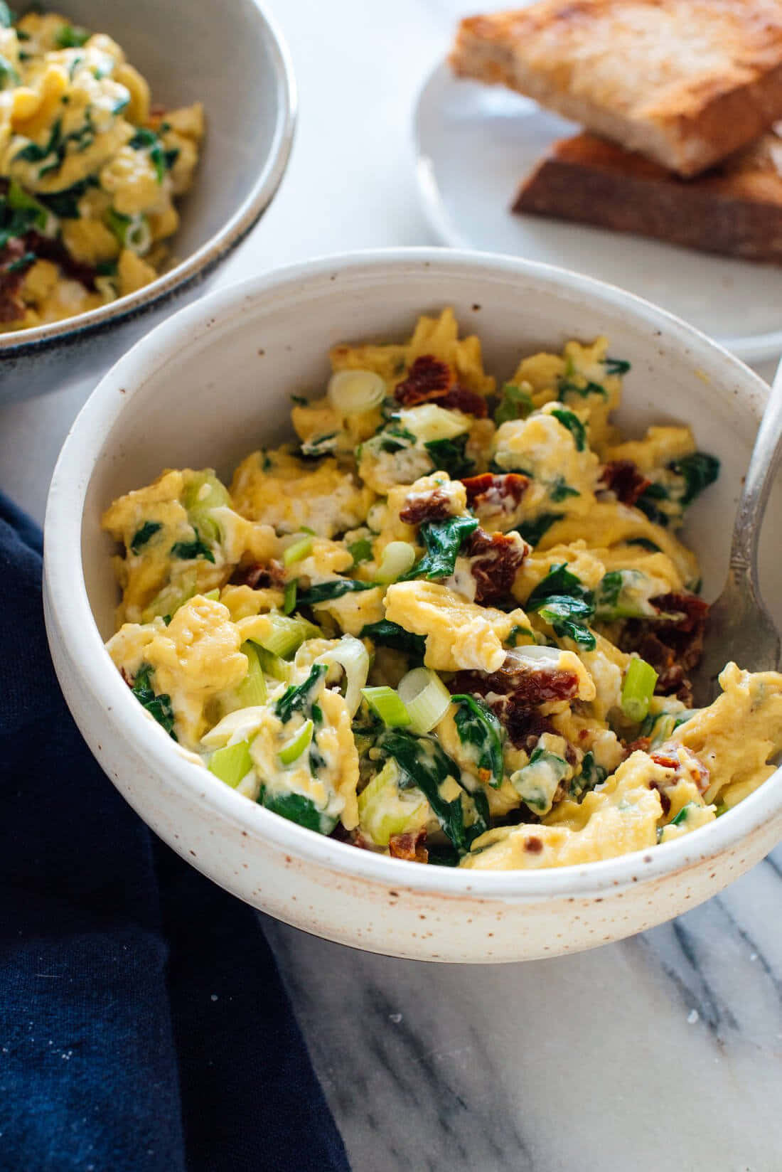 Scrambled Egg 桌布 壁紙 — 大理石檯面上一個有斑點的陶瓷碗中， fluffy 炒蛋配菠菜和曬乾番茄的特寫。