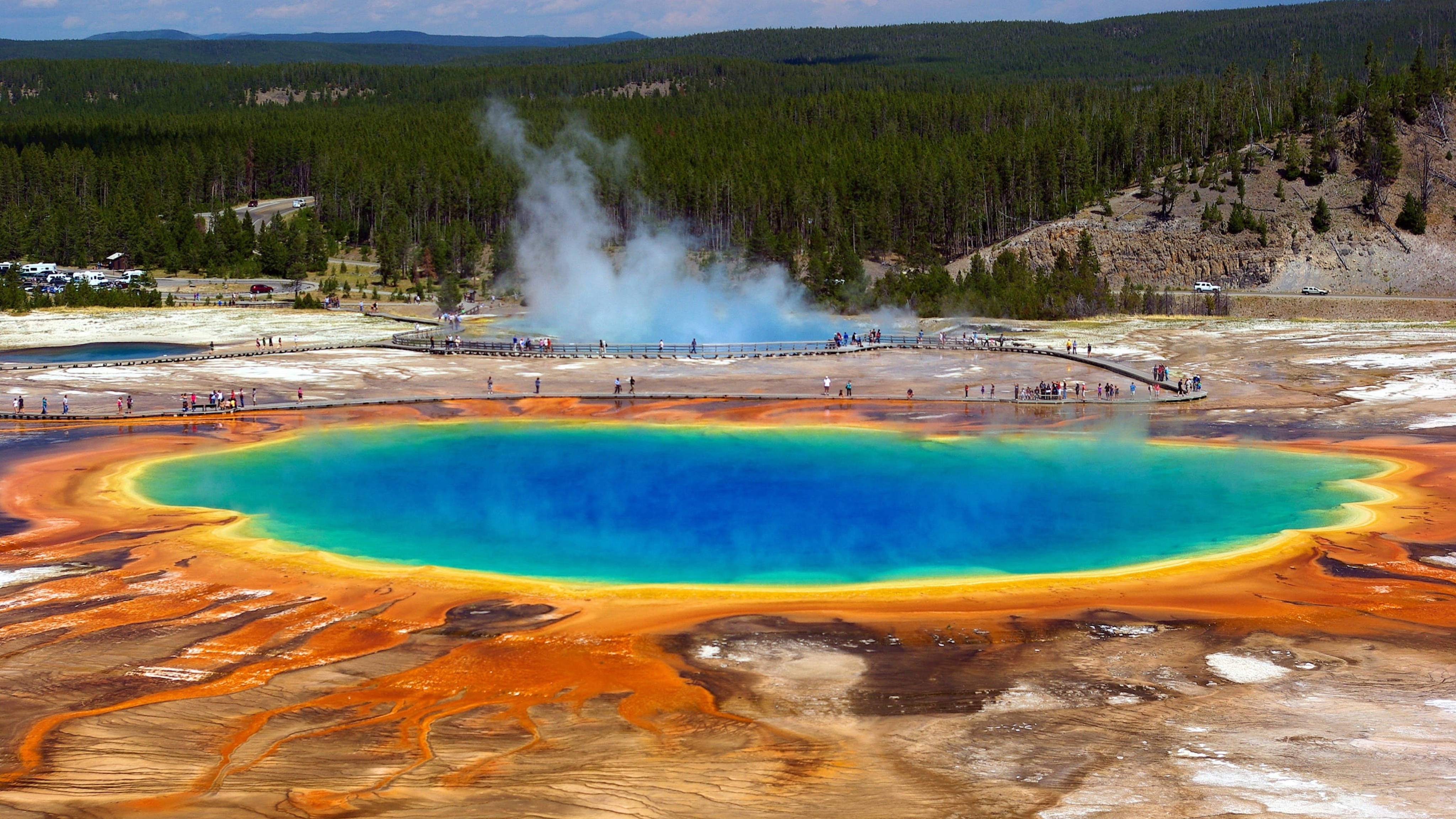 Yellowstone 桌布 壁紙 — 大稜鏡溫泉的航拍視圖，其鮮豔的藍色中心被橙色微生物墊包圍，遊客在木板路上。