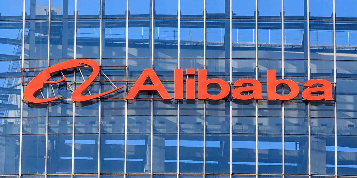 Alibaba 桌布 壁紙 — 大膽的橙色阿里巴巴標誌安裝在現代玻璃摩天大樓外牆上，反射藍天。