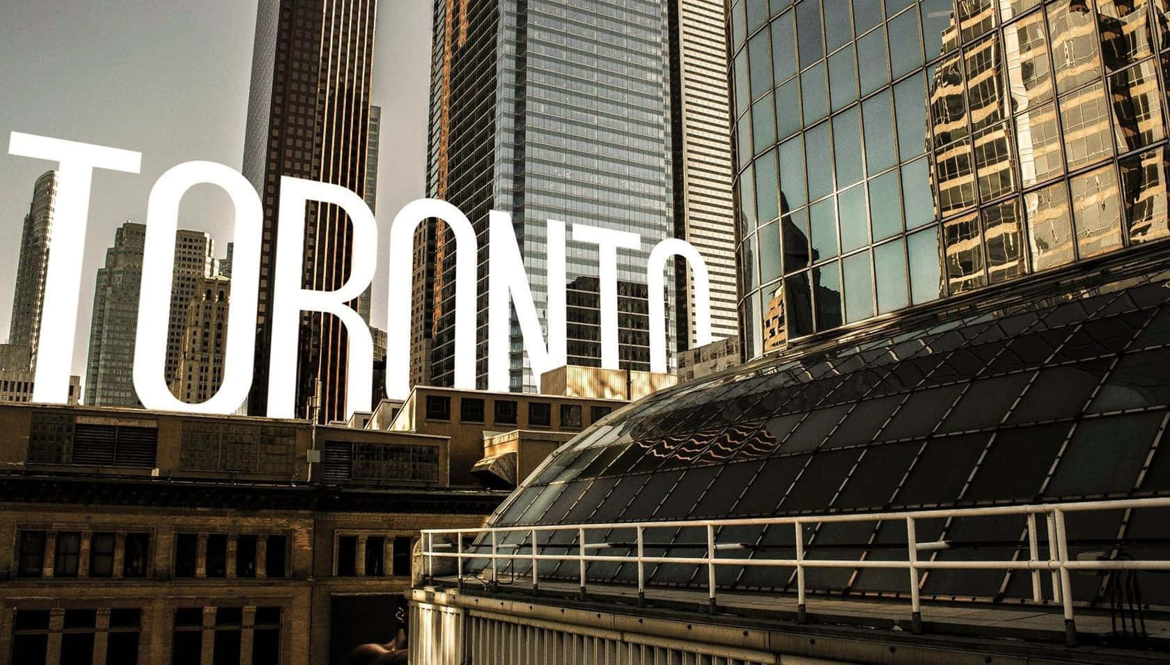 Toronto 桌布 壁紙 — 大膽的白色「TORONTO」字母在陽光普照的玻璃和鋼鐵摩天大樓城市景觀上方聳立。