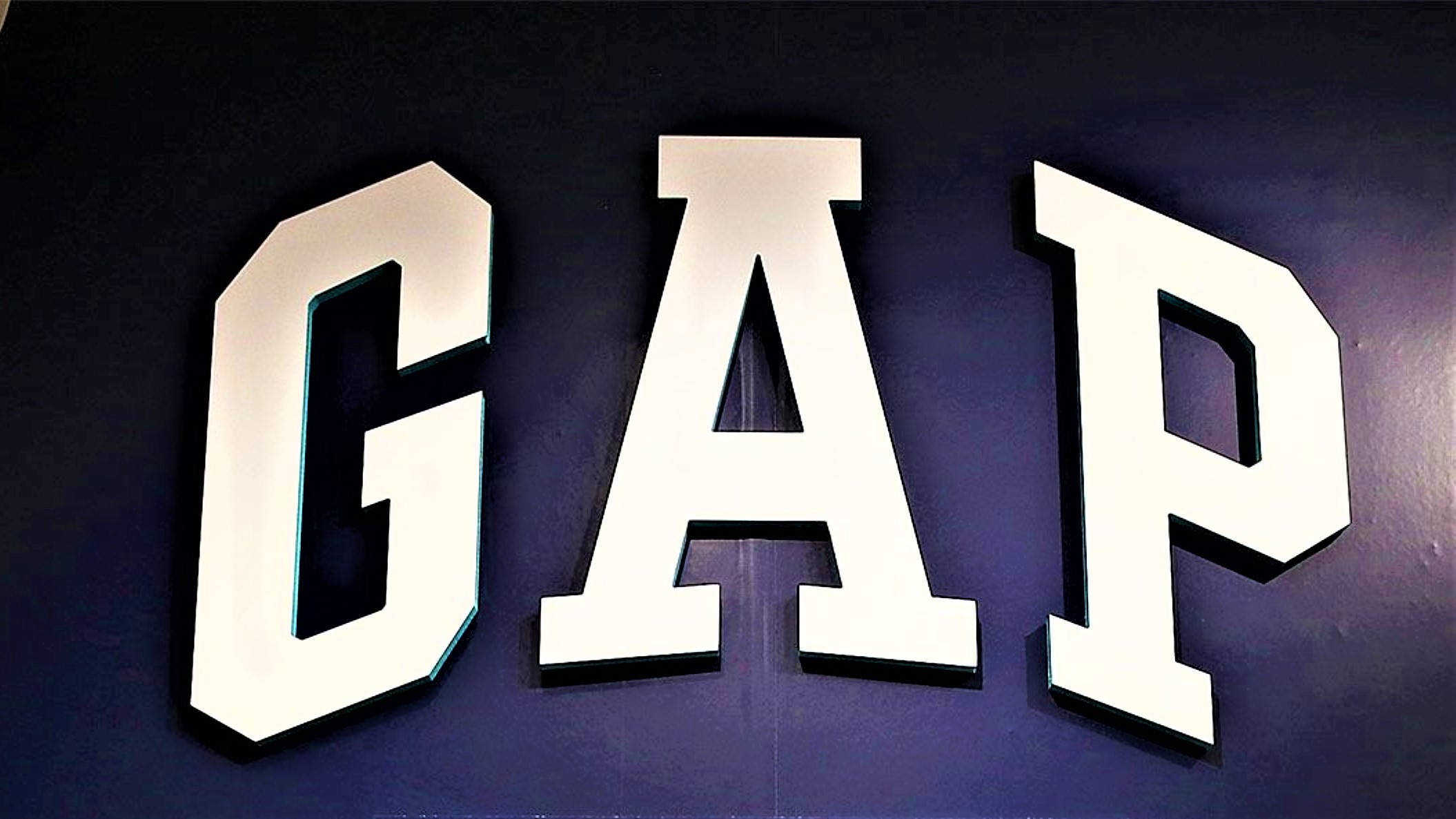 Gap 桌布 壁紙 — 大膽的白色3D GAP字母在深紫色牆壁上發光，營造出極簡主義的零售環境。