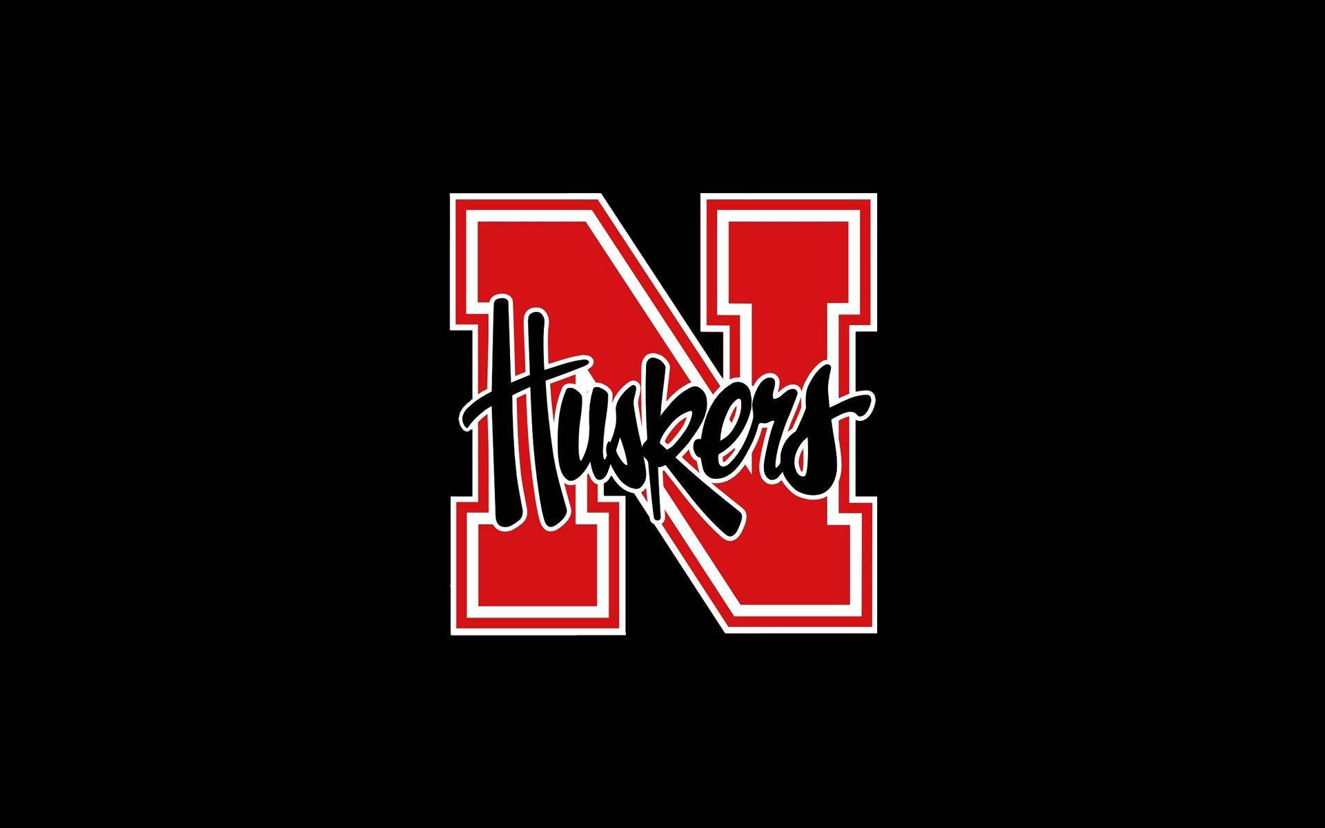 足球 桌布 壁紙 — 大膽的紅白 Huskers 標誌，黑色手寫字體居中，置於純黑色背景上。