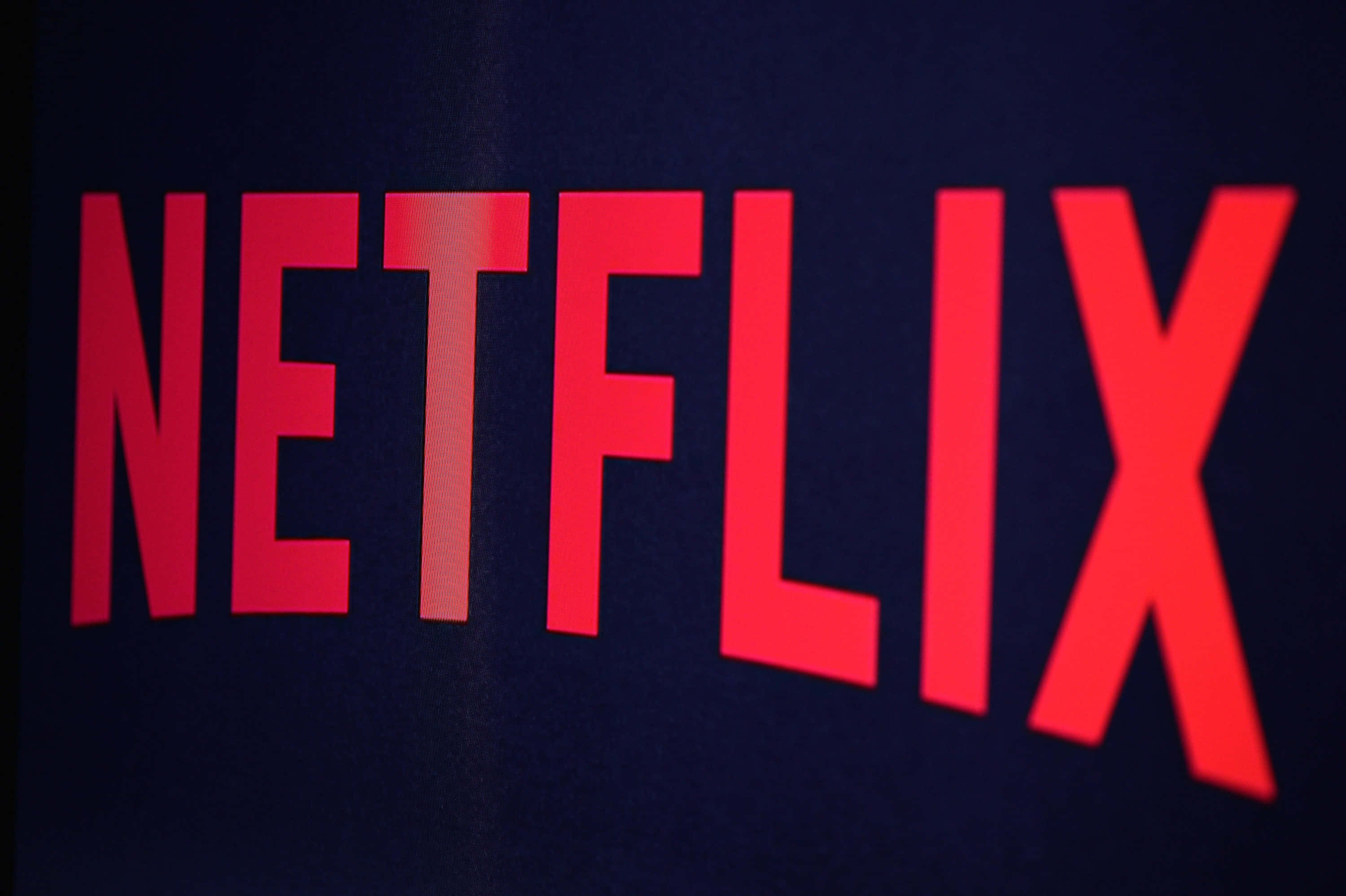 Netflix 桌布 壁紙 — 大膽的紅色 Netflix 標誌在深色紋理背景上發光，柔和的光線突出其邊緣。