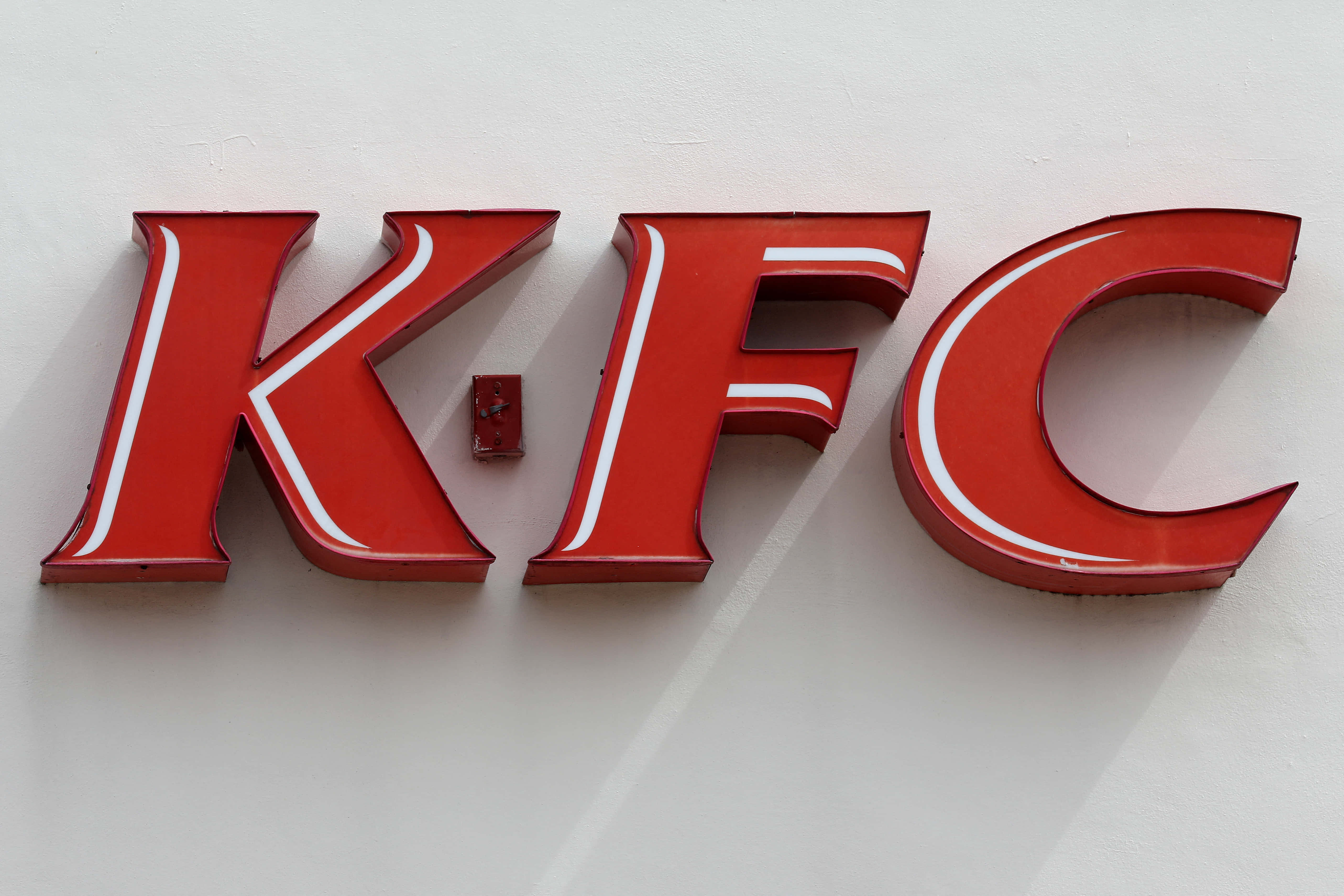 肯德基 桌布 壁紙 — 大膽的紅色3D KFC字母，帶有白色邊框，安裝在純白牆上，投射出柔和陰影。