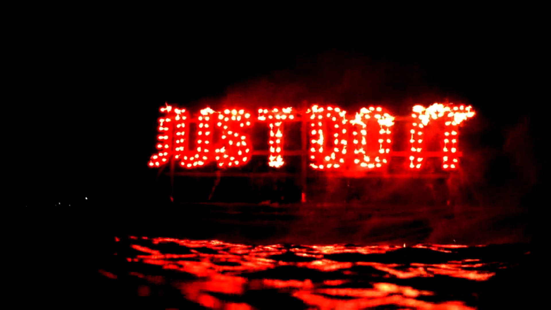 就去做吧 桌布 壁紙 — 大膽的紅色LED字母拼出JUST DO IT，在黑暗的夜空中強烈發光，下方濕漉漉的地面上反射出閃爍的光芒。