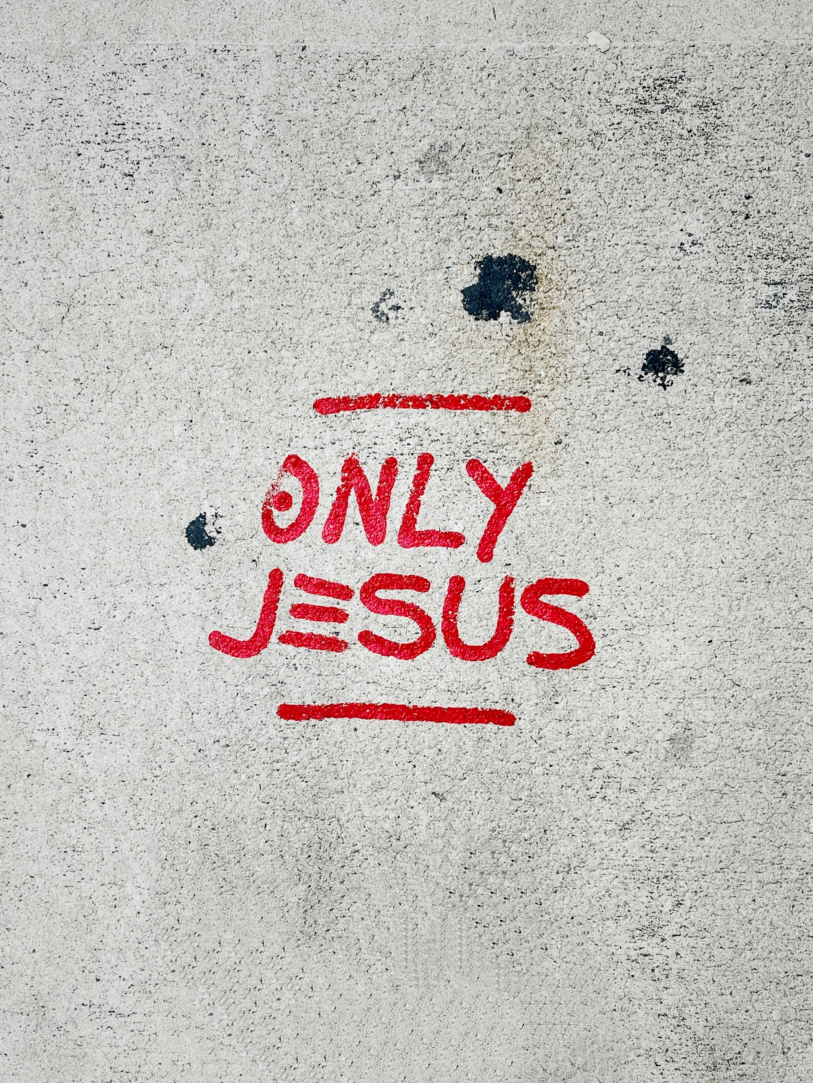 Jesus Name 桌布 壁紙 — 大膽的紅色塗鴉在風化的灰色混凝土上寫著「only jesus」，並帶有散落的深色污漬。