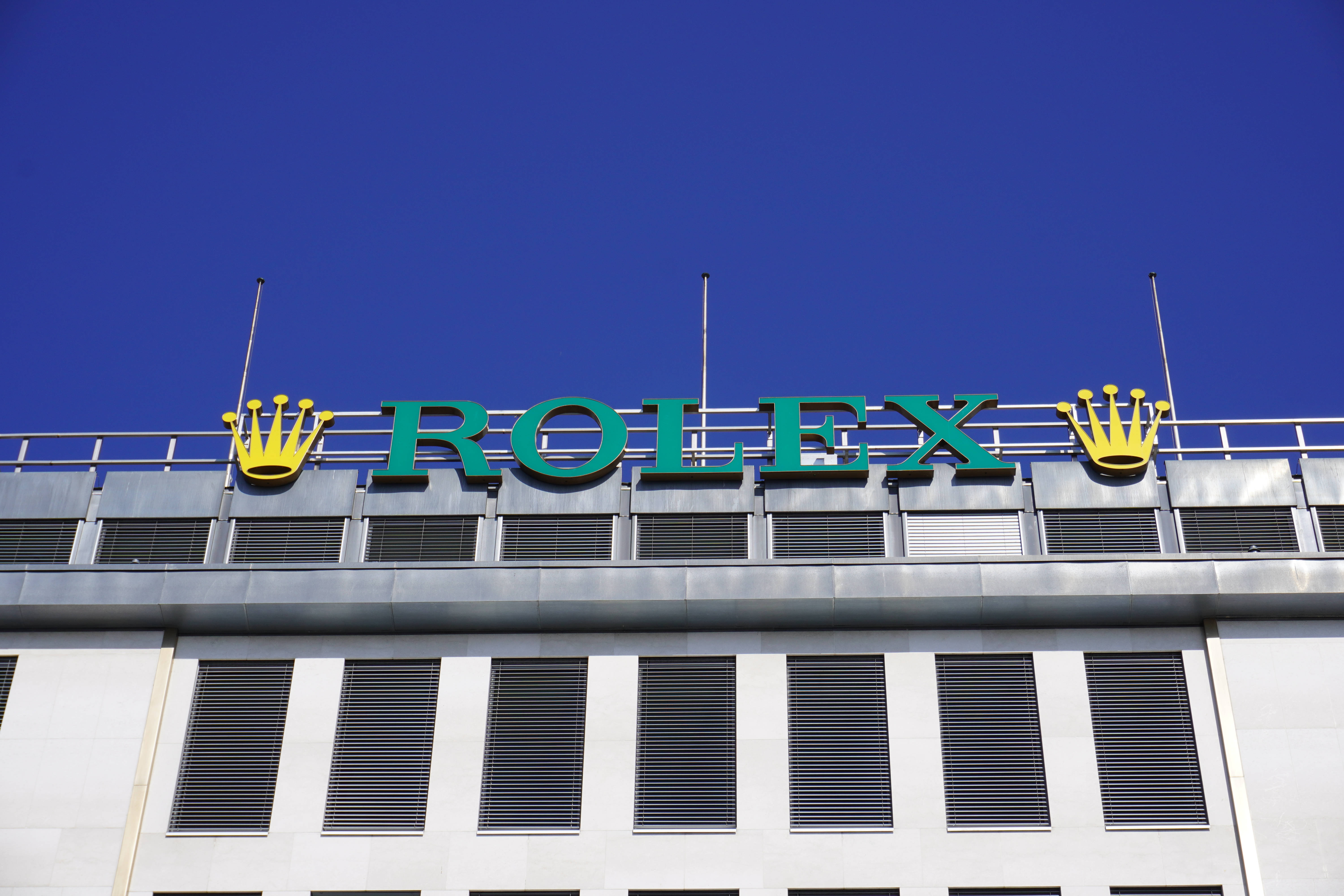 Rolex 桌布 壁紙 — 大膽的綠色勞力士標誌，金色皇冠矗立於現代建築之上，背景是清澈的藍天。