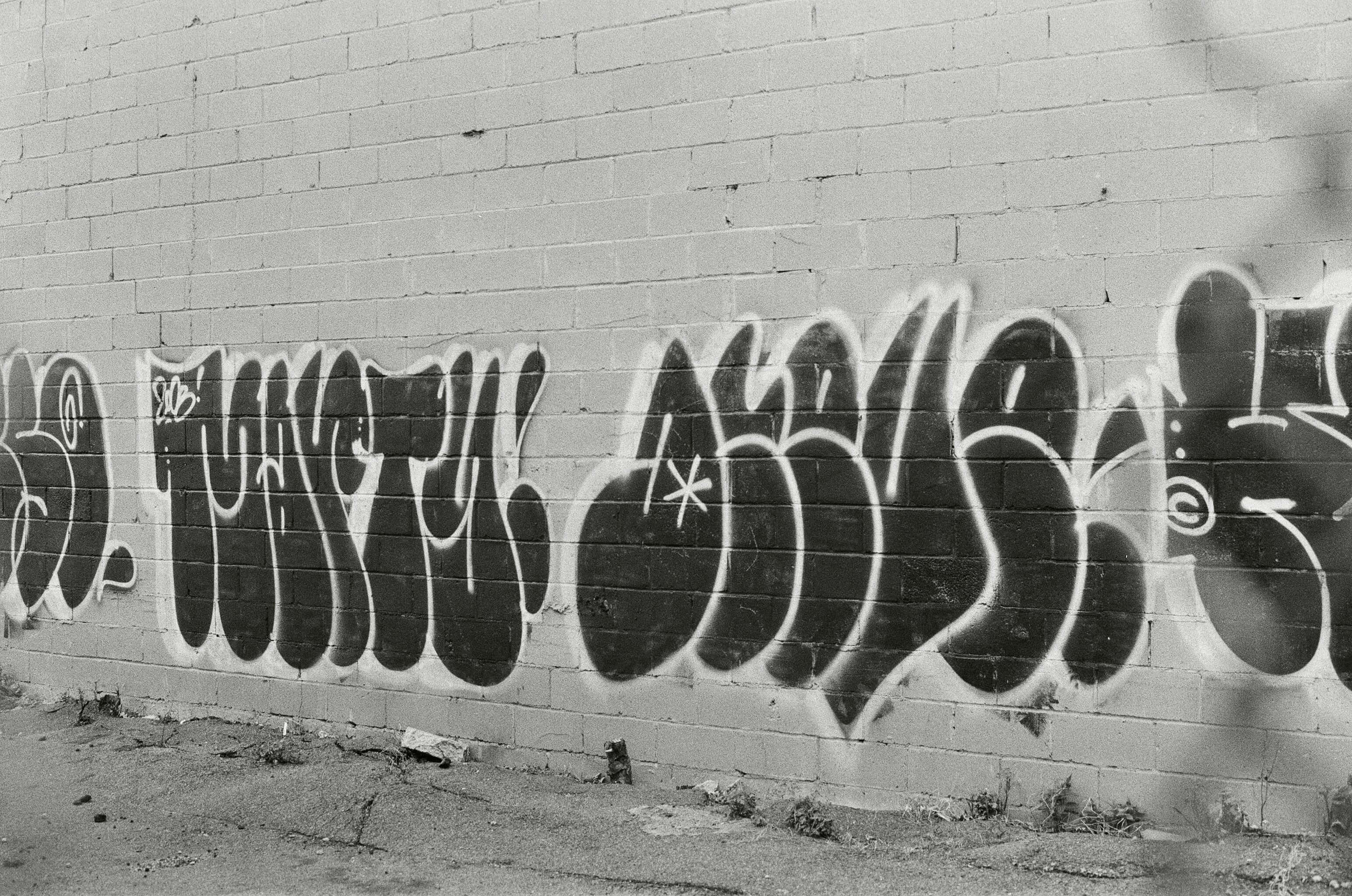 Black And White Graffiti 桌布 壁紙 — 大膽的黑白塗鴉標記在風化的磚牆上蔓延，呈現出粗獷的城市衰敗景象。