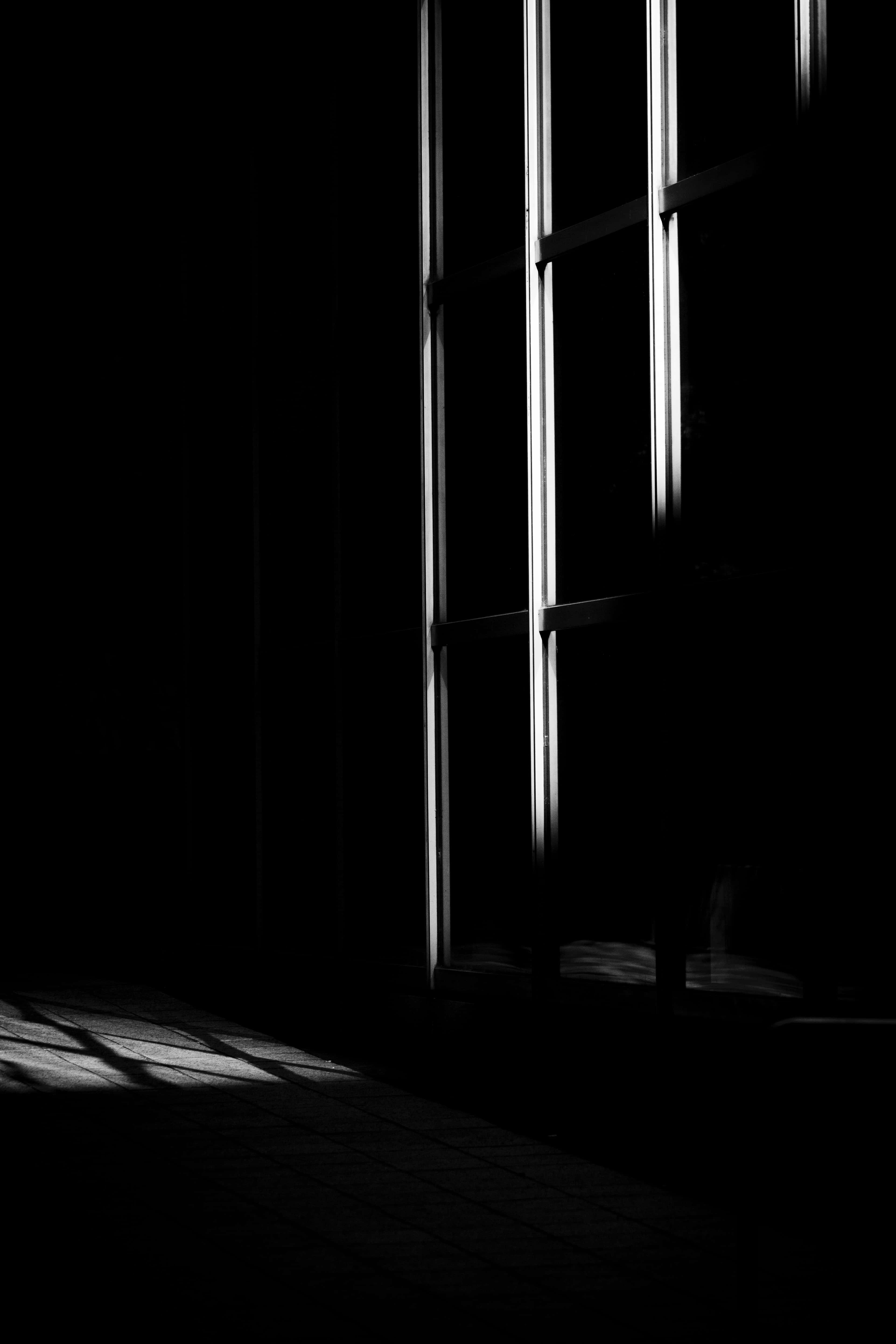 Dark Room 桌布 壁紙 — 大膽的黑白照片，垂直的窗欄在深暗陰影中的瓷磚地板上投射出銳利的光束。