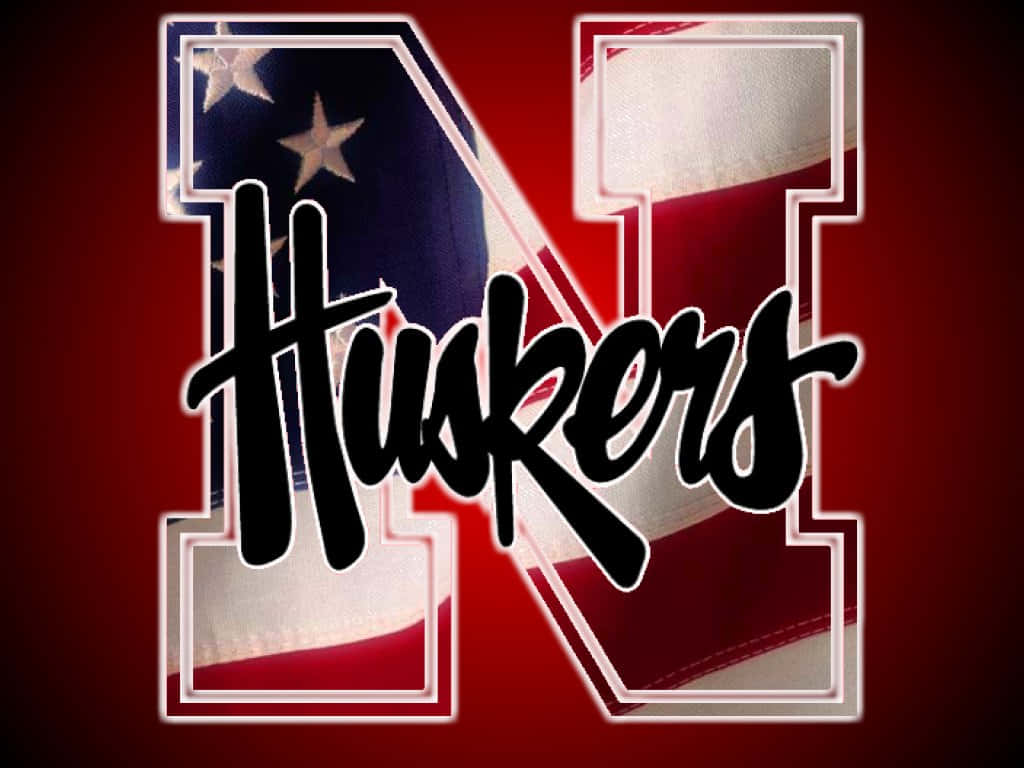 桌布 壁紙 — 大膽的黑色 'Huskers' 字體覆蓋在一個大型風格化 'N' 上，該 'N' 填充了美國國旗布料，背景為深紅色。
