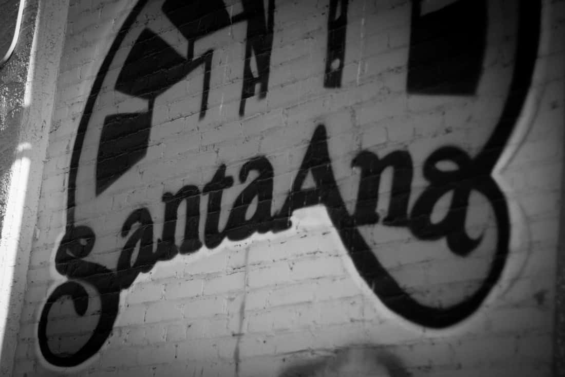藝術 桌布 壁紙 — 大膽的黑色塗鴉拼出 Santa Ana，以高對比黑白蜿蜒穿過風化的磚牆。
