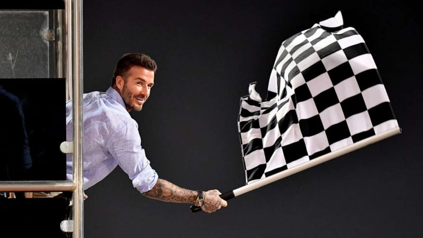 Chequered Flag 桌布 壁紙 — 大衛貝克漢在黑暗背景的攤位中微笑揮動格子賽車旗。