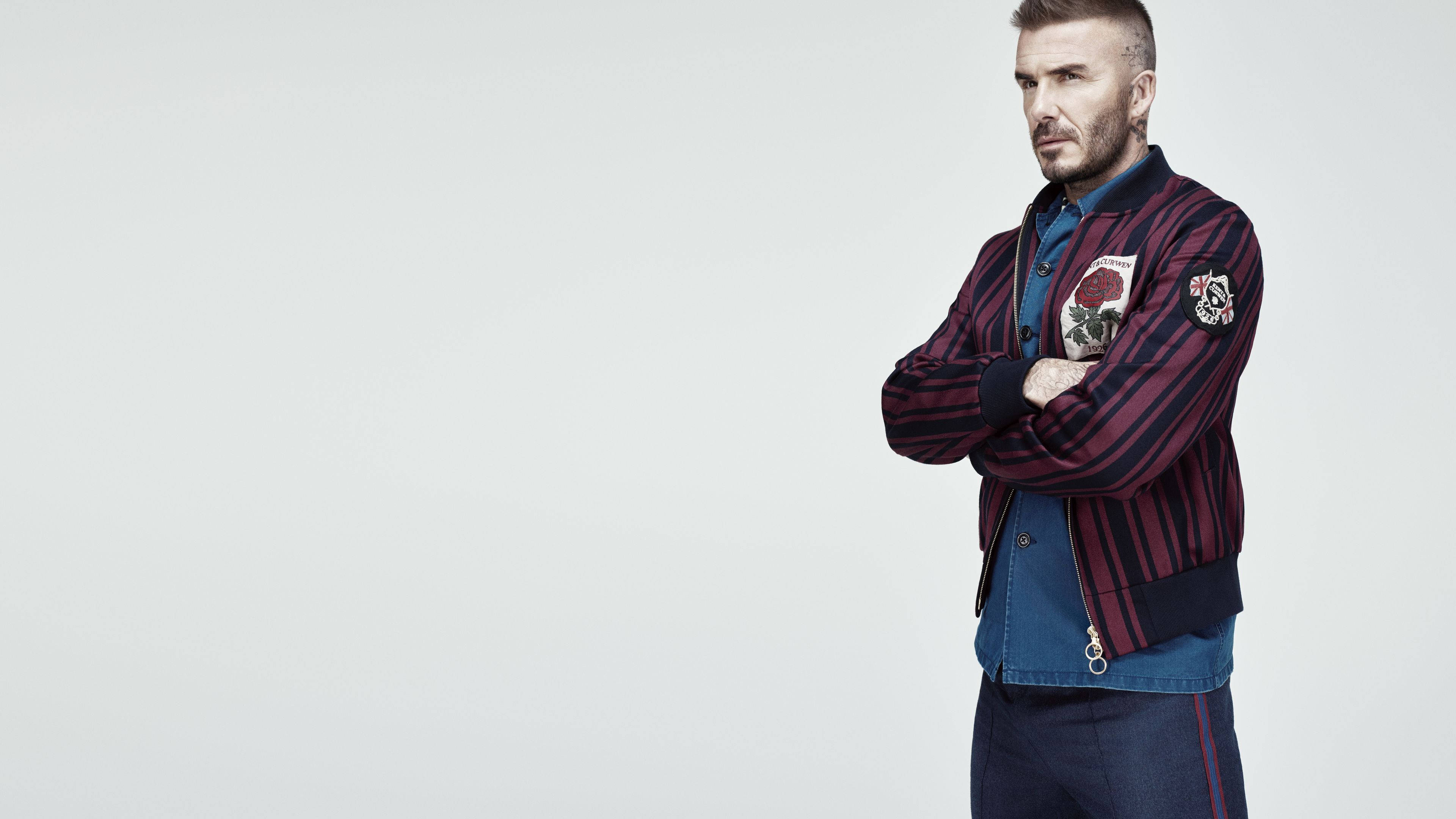 David Beckham 桌布 壁紙 — 大衛貝克漢自信地交叉雙臂，身穿條紋飛行員夾克，背景為純白色。