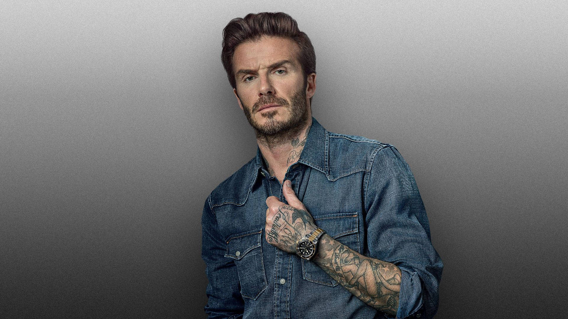 大衛·貝克漢 桌布 壁紙 — 大衛貝克漢身穿牛仔襯衫，在漸變灰色背景前自信擺姿勢，露出紋身和手錶。