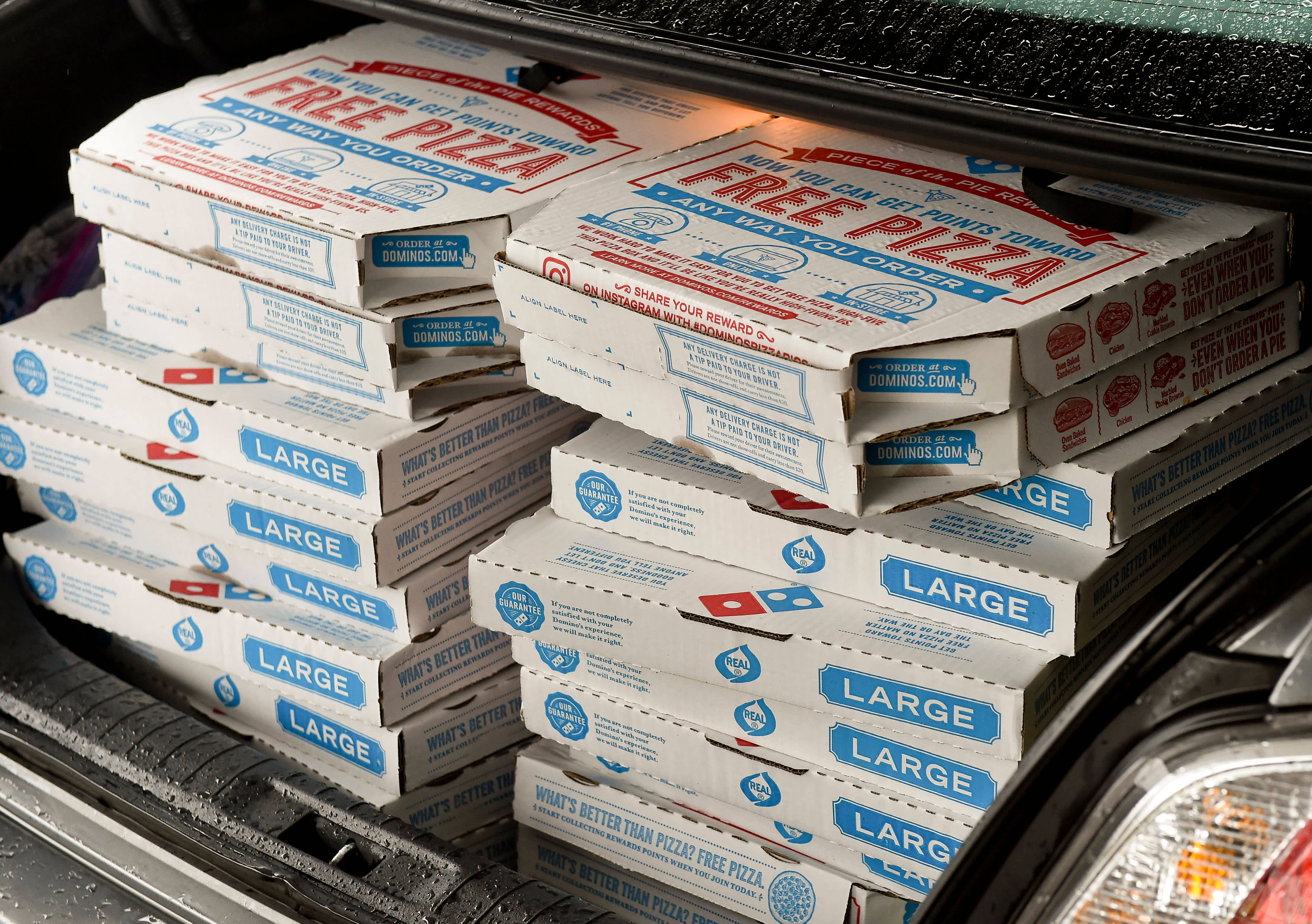 Box 桌布 壁紙 — 大量Domino's大型披薩盒堆滿汽車後車廂，帶有醒目的紅、藍、白品牌標誌。