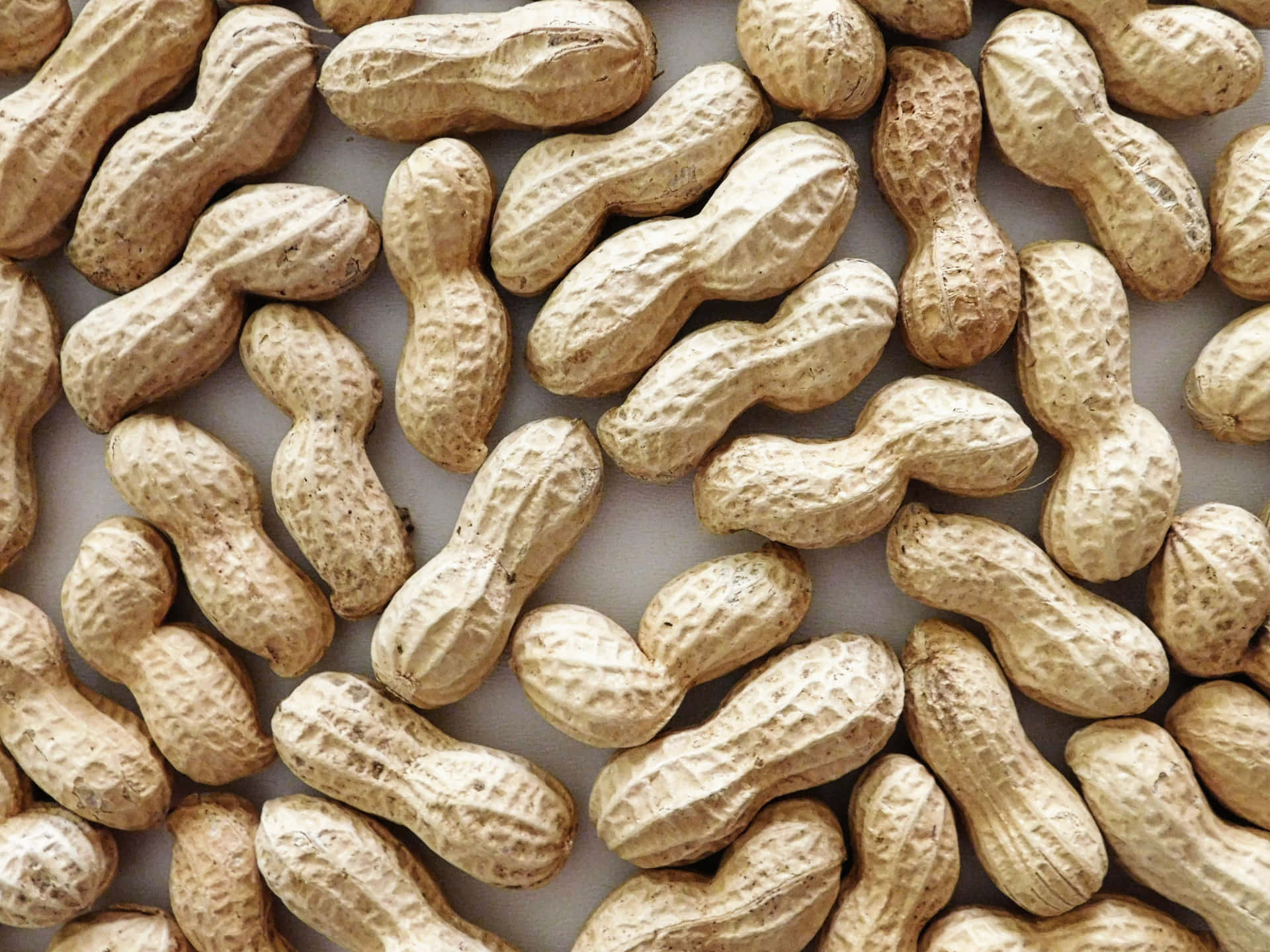 Peanuts 壁紙 — 大量帶有紋理的米色外殼生花生散落在平面表面上的特寫。