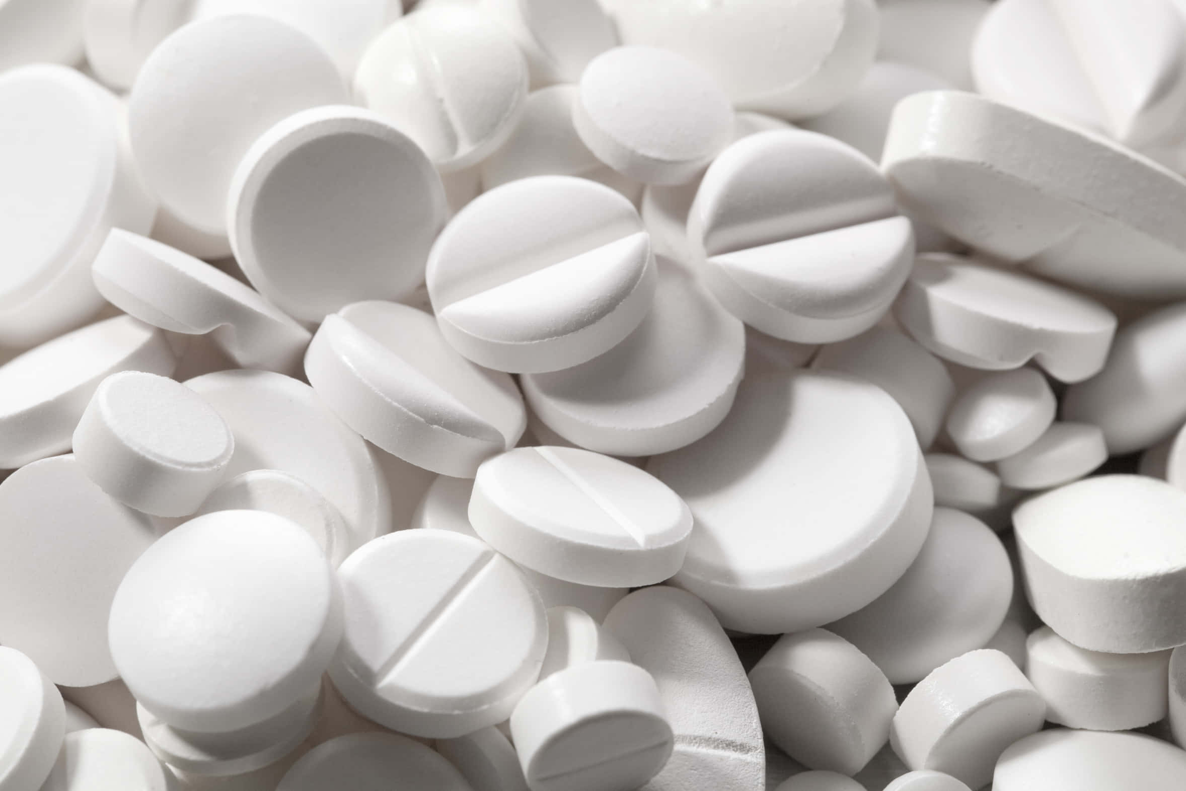 pills 桌布 壁紙 — 大量白色藥丸密集散落的特寫，帶有銳利陰影和光滑表面。
