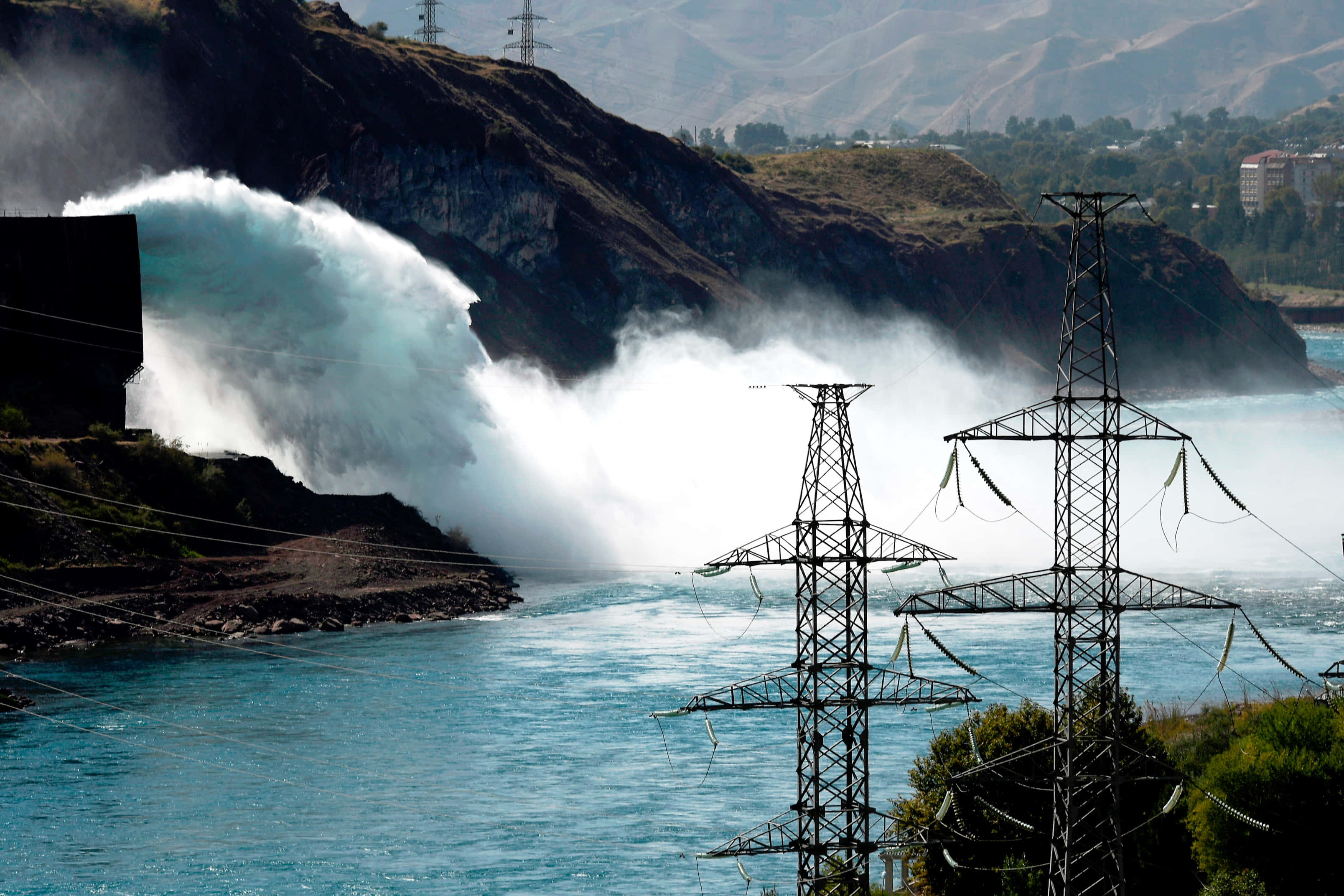 Energy 桌布 壁紙 — 大量藍綠色水從水壩溢洪道傾瀉而下，將水霧送入空中，而電線則聳立在下方河流之上。